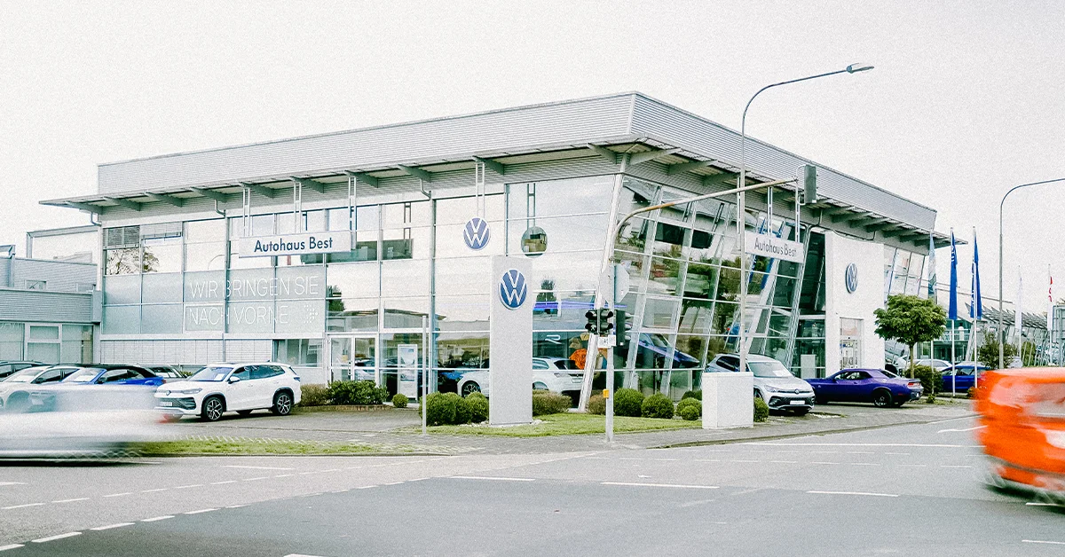 Eine Aufnahme des Volkswagen Autohauses in Mühlheim am Main, die das Gebäude und Volkswagen Fahrzeuge vor dem Gebäude, sowie Parkplätze zeigt.