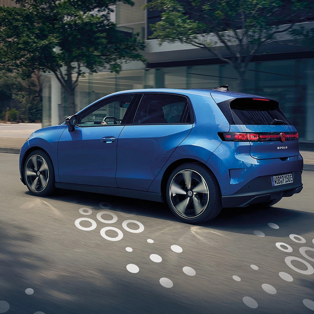 Ein blauer Volkswagen ID. Polo fährt durch eine moderne Stadtstraße. Das Heck und die Seite des Fahrzeugs sind zu sehen, während weiße Kreisgrafiken auf dem Asphalt Dynamik andeuten.