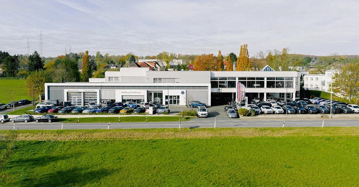 Eine Aufnahme des Volkswagen Autohauses in Hofheim am Taunus, die das Gebäude und Volkswagen Fahrzeuge vor dem Gebäude, sowie die Einfahrt und die Rheingaustraße zeigt.