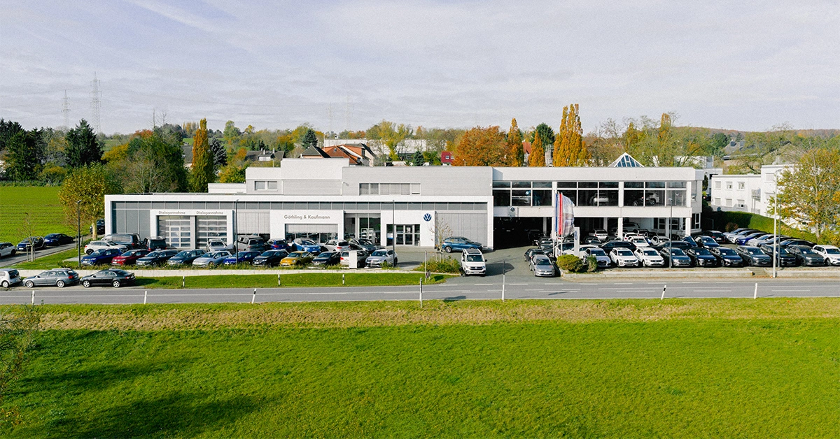 Eine Aufnahme des Volkswagen Autohauses in Hofheim am Taunus, die das Gebäude und Volkswagen Fahrzeuge vor dem Gebäude, sowie die Einfahrt und die Rheingaustraße zeigt.