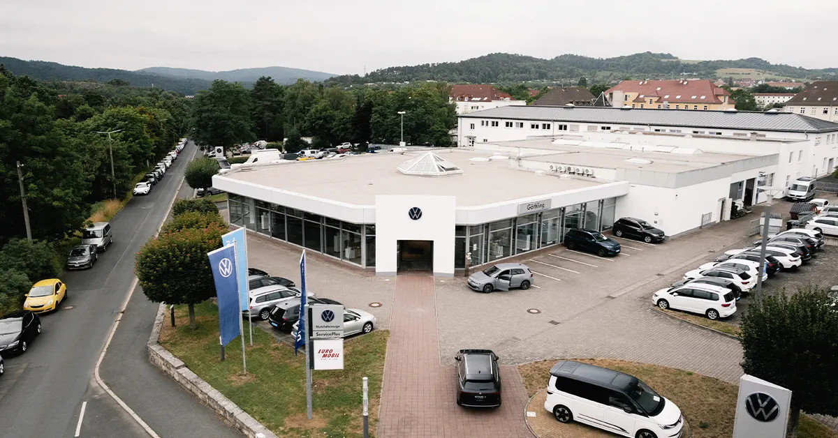 Eine Aufnahme des Volkswagen und Volkswagen Nutzfahrzeuge Autohauses in Eisenach, die das Gebäude und Volkswagen Fahrzeuge vor dem Gebäude, sowie die Einfahrt zeigt.