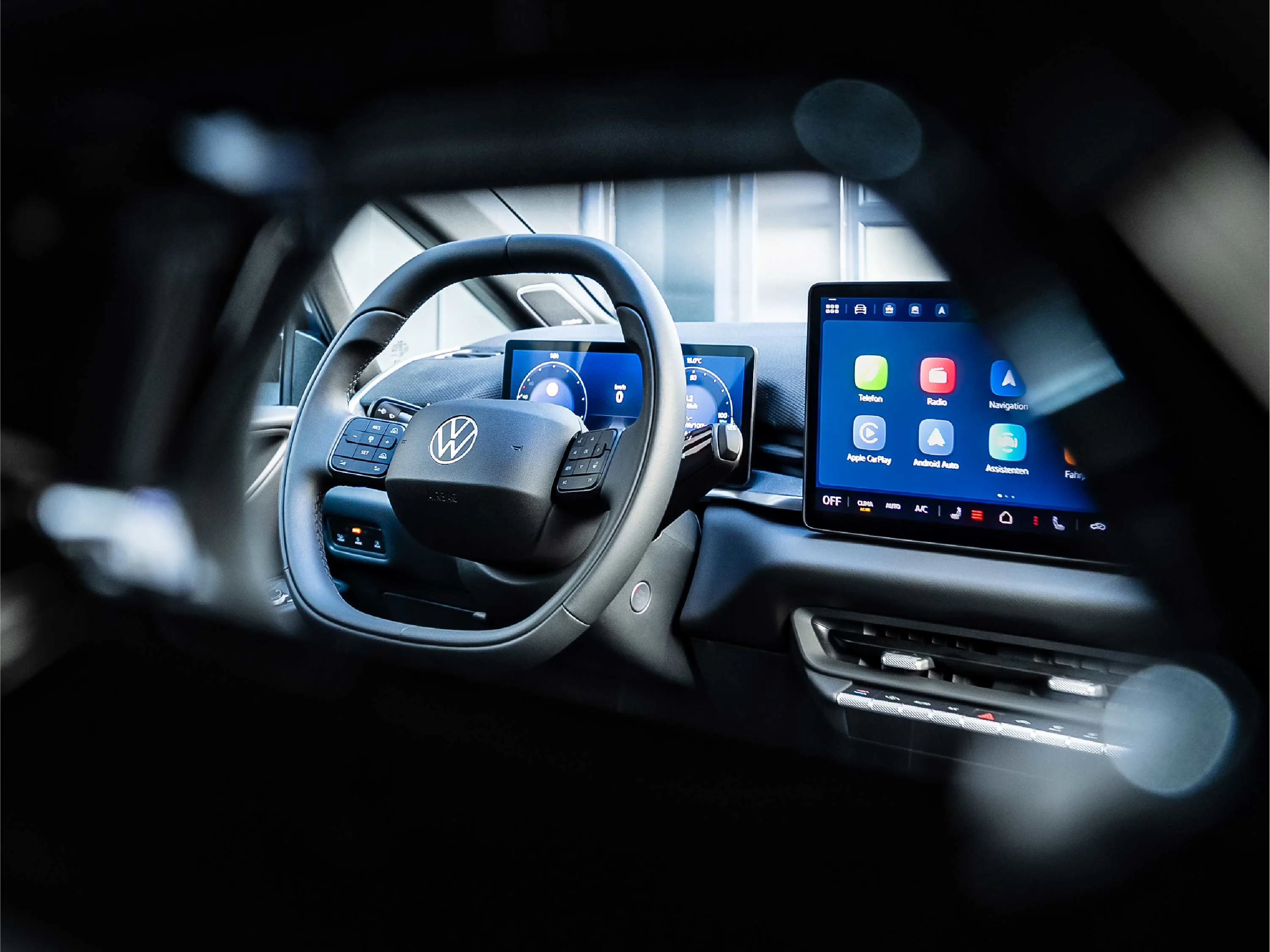 Blick durch das Lenkrad auf das digitale Cockpit eines VW ID.3. Das Infotainment-Display zeigt verschiedene App-Kacheln wie Apple CarPlay und Navigation. Die Gestaltung wirkt durch die selektive Schärfe modern und technikfokussiert.