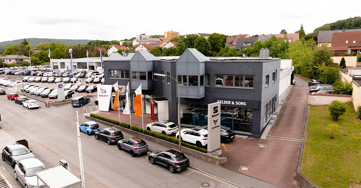 Eine Aufnahme des SEAT und CUPRA Autohauses in Lichtenfels, die das Gebäude und Fahrzeuge vor dem Gebäude, sowie die Grünewaldstraße und die Einfahrt zeigt.