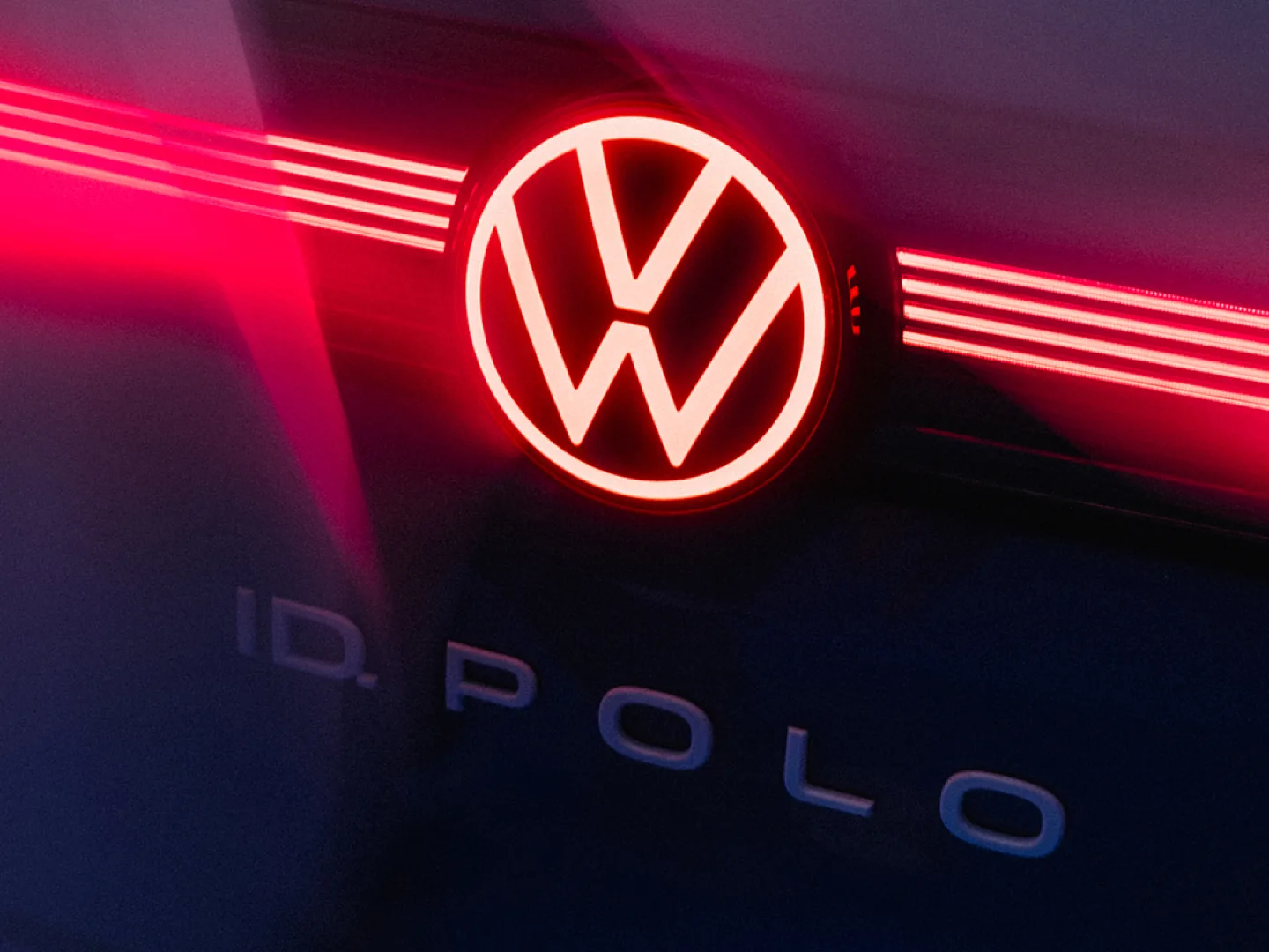 Nahaufnahme des Hecks eines VW ID.Polo. Zu sehen ist das rot leuchtende VW-Logo, das in ein horizontales LED-Lichtband übergeht, sowie der markante „ID. POLO“-Schriftzug auf der dunklen Karosserie.