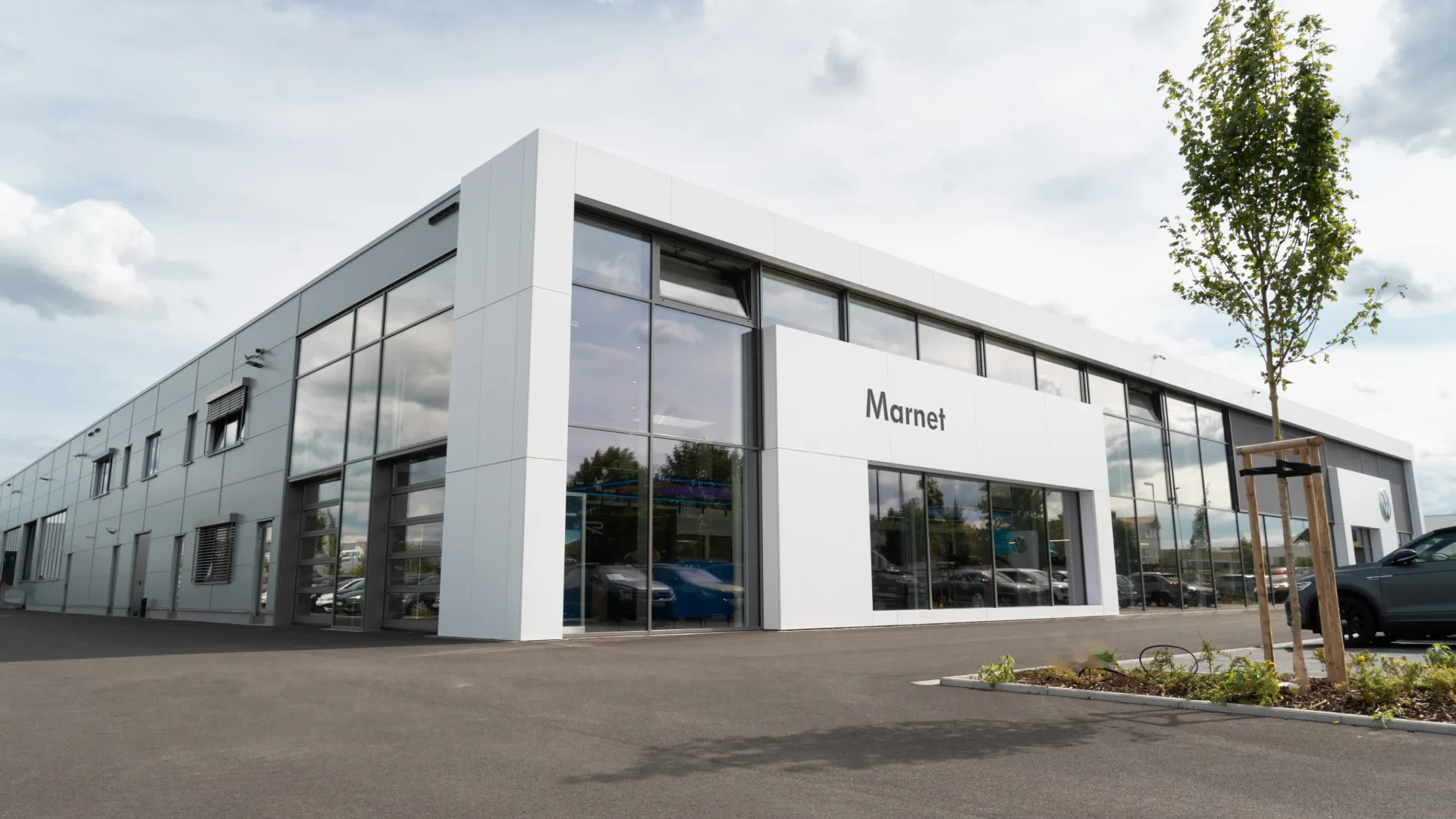 Eine Aufnahme des Volkswagen Autohauses in Wiesbaden, dass das Gebäude und Volkswagen Fahrzeuge vor dem Gebäude, sowie die Einfahrt zeigt.