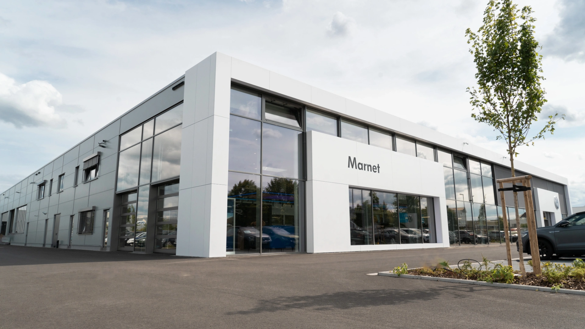 Eine Aufnahme des Volkswagen Autohauses in Wiesbaden, dass das Gebäude und Volkswagen Fahrzeuge vor dem Gebäude, sowie die Einfahrt zeigt.