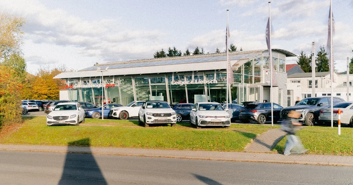 Eine Aufnahme des Audi Gebrauchtwagen :plus Autohauses in Linsengericht, die das Gebäude und Audi Fahrzeuge vor dem Gebäude, sowie die Gelnhäuser Straße zeigt.