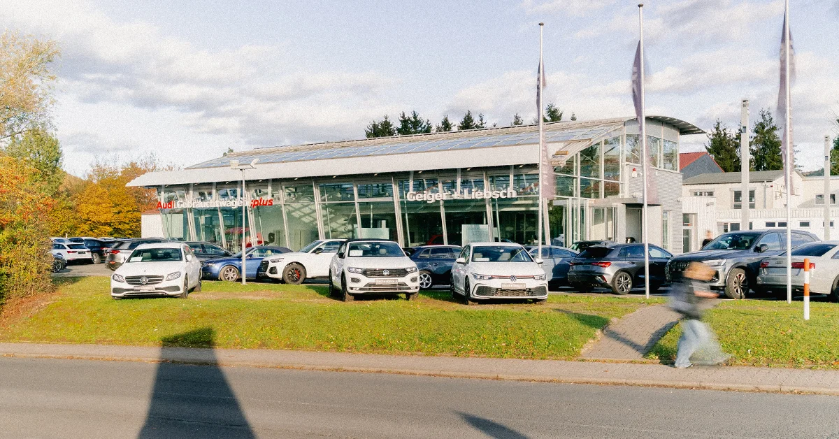 Eine Aufnahme des Audi Gebrauchtwagen :plus Autohauses in Linsengericht, die das Gebäude und Audi Fahrzeuge vor dem Gebäude, sowie die Gelnhäuser Straße zeigt.