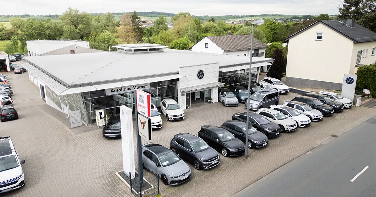 Eine Aufnahme des Volkswagen Autohauses in Bad Camberg, die das Gebäude und Volkswagen Fahrzeuge vor dem Gebäude, sowie die Einfahrt zeigt.