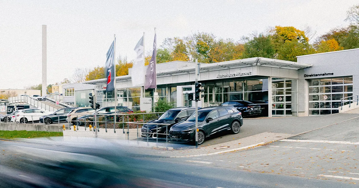 Eine Aufnahme des Audi Autohauses in Königstein im Taunus, die das Gebäude und Audi Fahrzeuge vor dem Gebäude, sowie die Einfahrt zeigt.