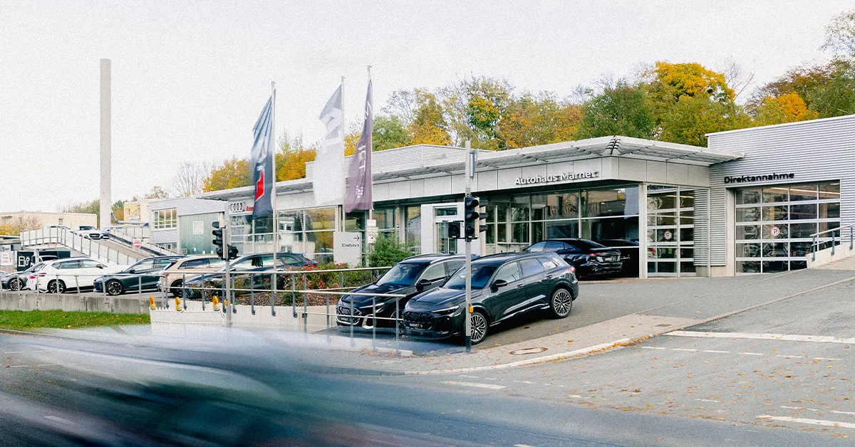 Eine Aufnahme des Audi Autohauses in Königstein im Taunus, die das Gebäude und Audi Fahrzeuge vor dem Gebäude, sowie die Einfahrt zeigt.