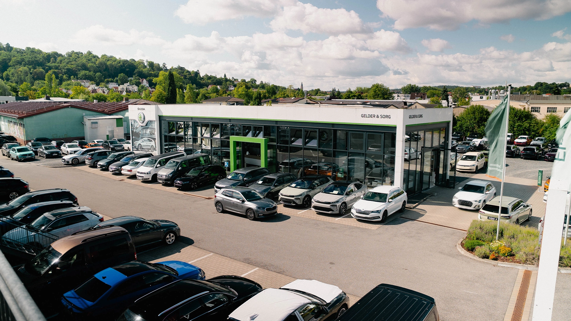 Škoda Coburg Header Eine Aufnahme des Škoda Autohauses in Coburg, dass den Haupteingang des Gebäudes, einen Teil des Hofes und Škoda Fahrzeuge zeigt.