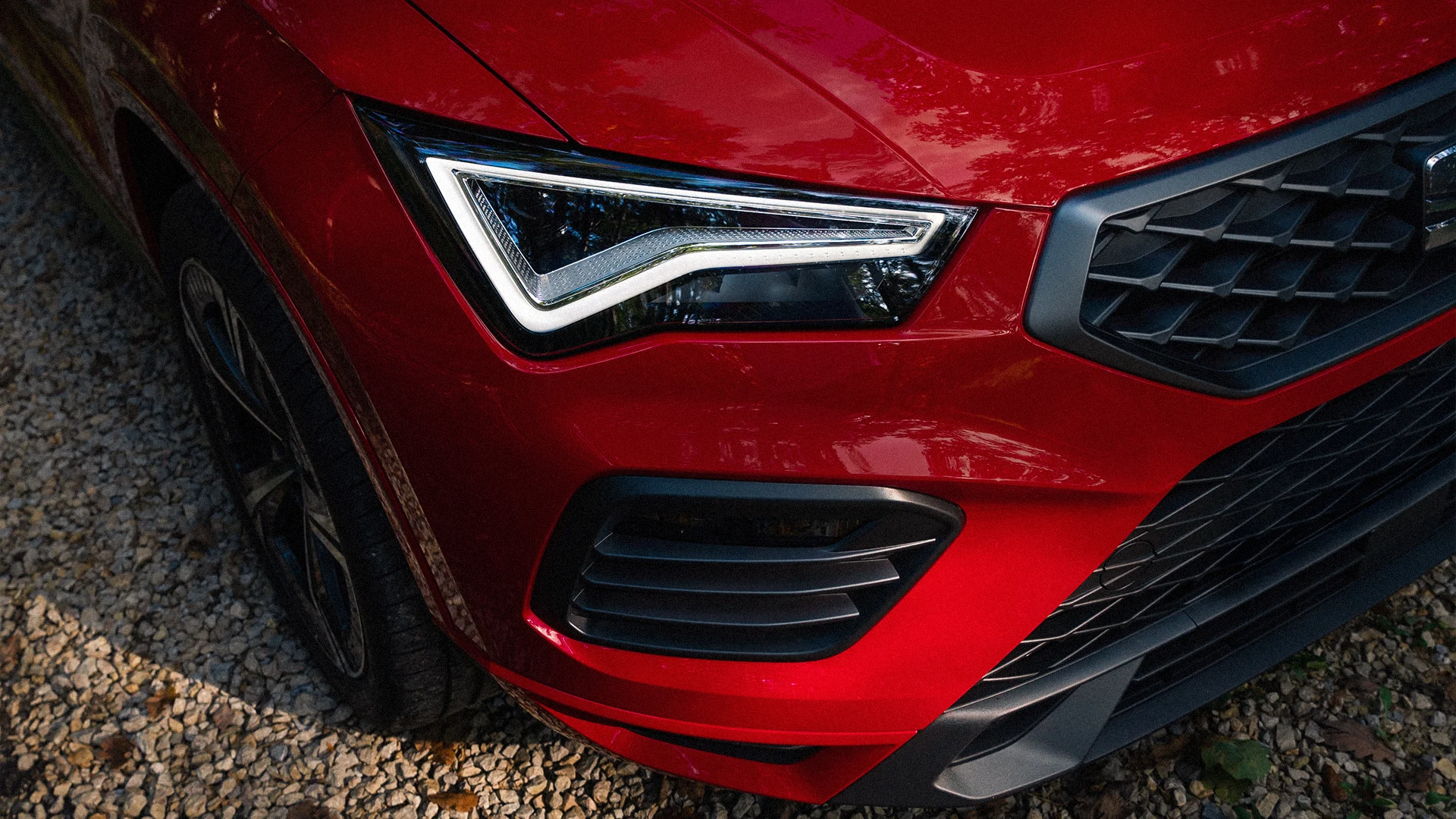 Eine Aufnahme des vorderen Scheinwerfers eines roten SEAT Fahrzeuges, am Boden liegt Kies.