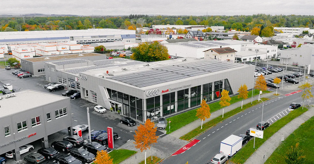 Eine Aufnahme des Audi Zentrum Autohauses in Hanau, die das Gebäude und Audi Fahrzeuge vor dem Gebäude, sowie die Einfahrt zeigt.