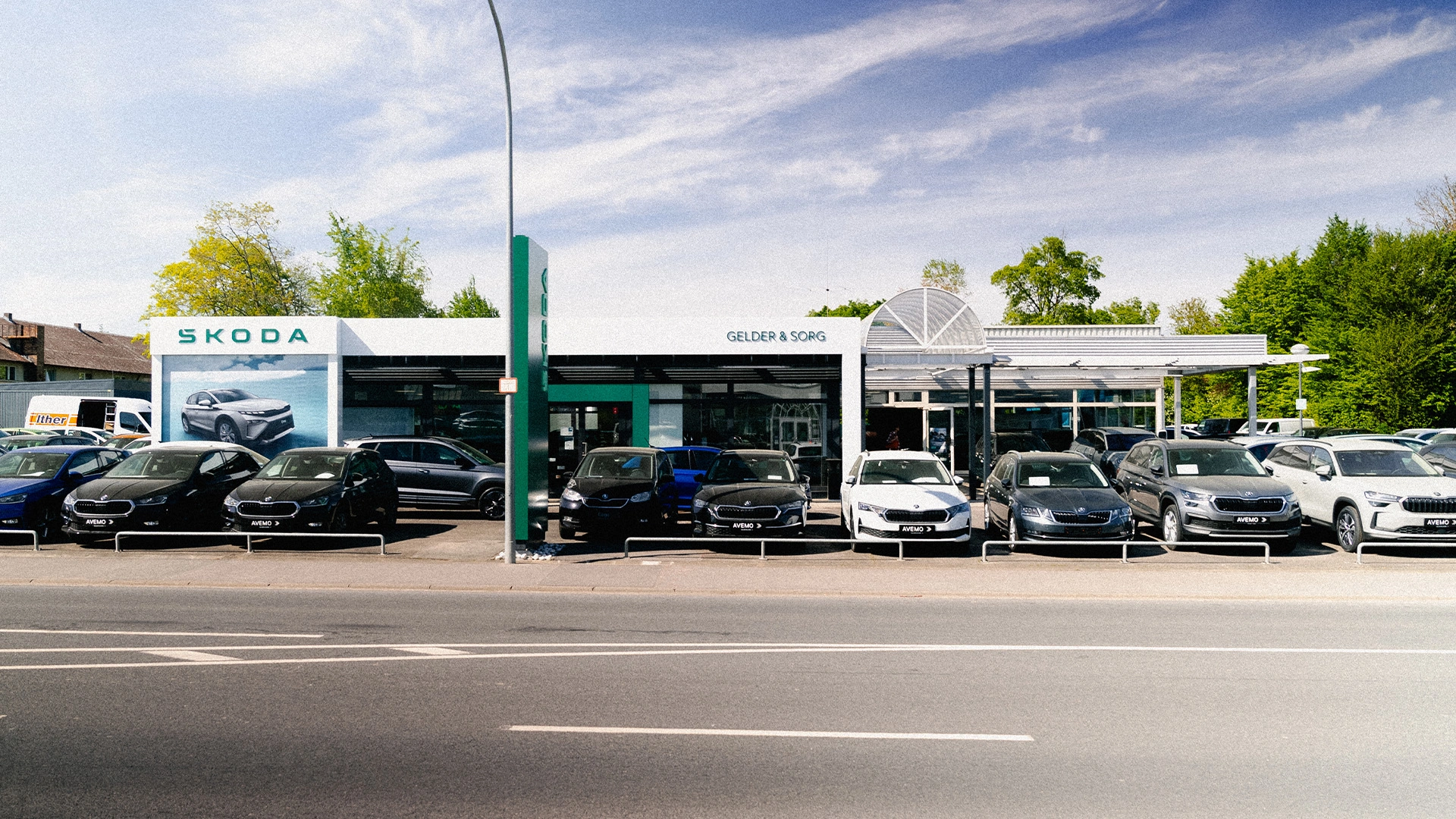 Eine Aufnahme des Škoda Autohauses in Haßfurt, die das Gebäude, den Haupteingang  sowie die Škoda Fahrzeuge vor dem Autohaus zeigt.