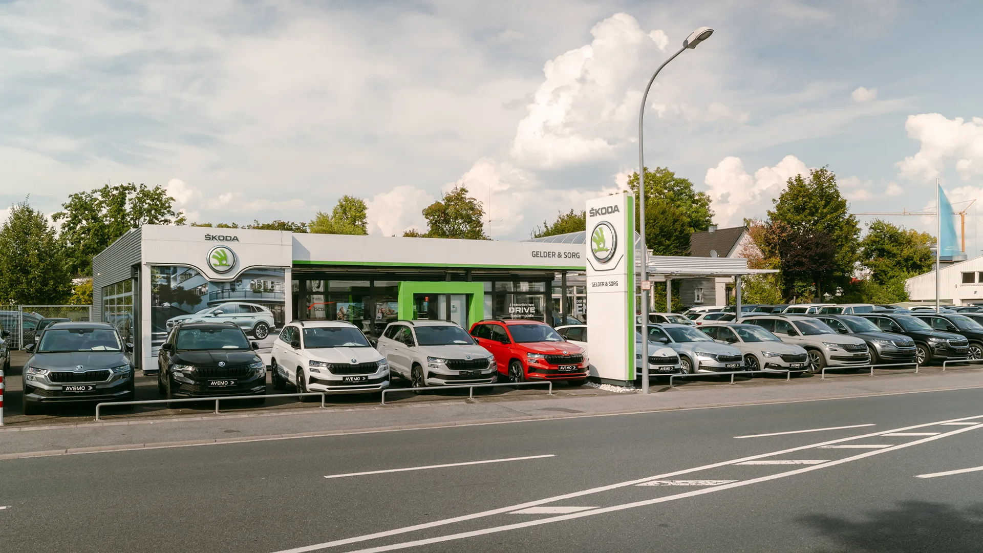 Eine Aufnahme des Škoda Autohauses in Haßfurt, die das Gebäude, den Haupteingang  sowie die Škoda Fahrzeuge vor dem Autohaus zeigt.