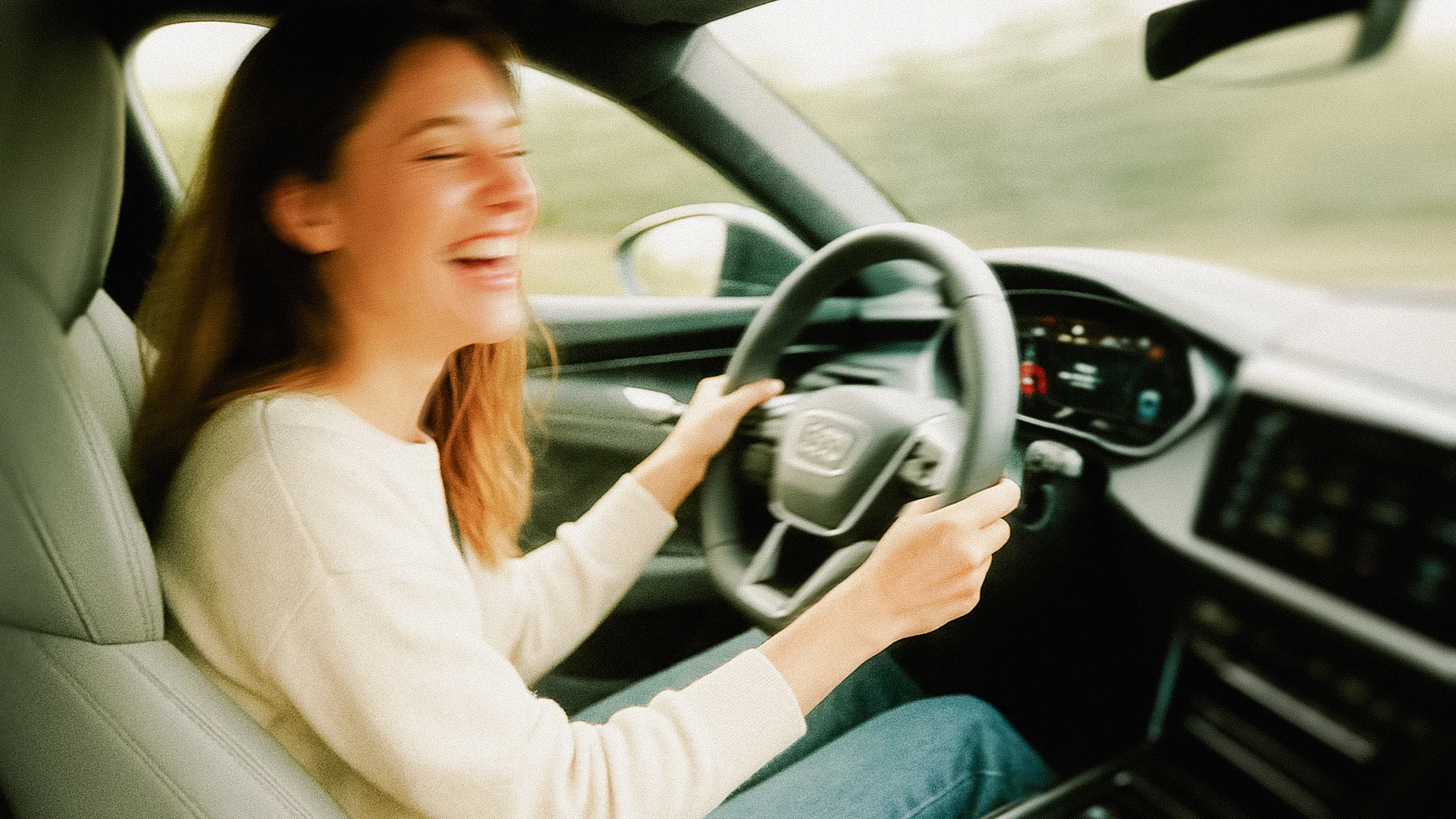 Eine unscharfe Aufnahme einer lachenden, brunetten Frau, die am Steuer eines Audi Fahrzeugs sitzt und fährt.