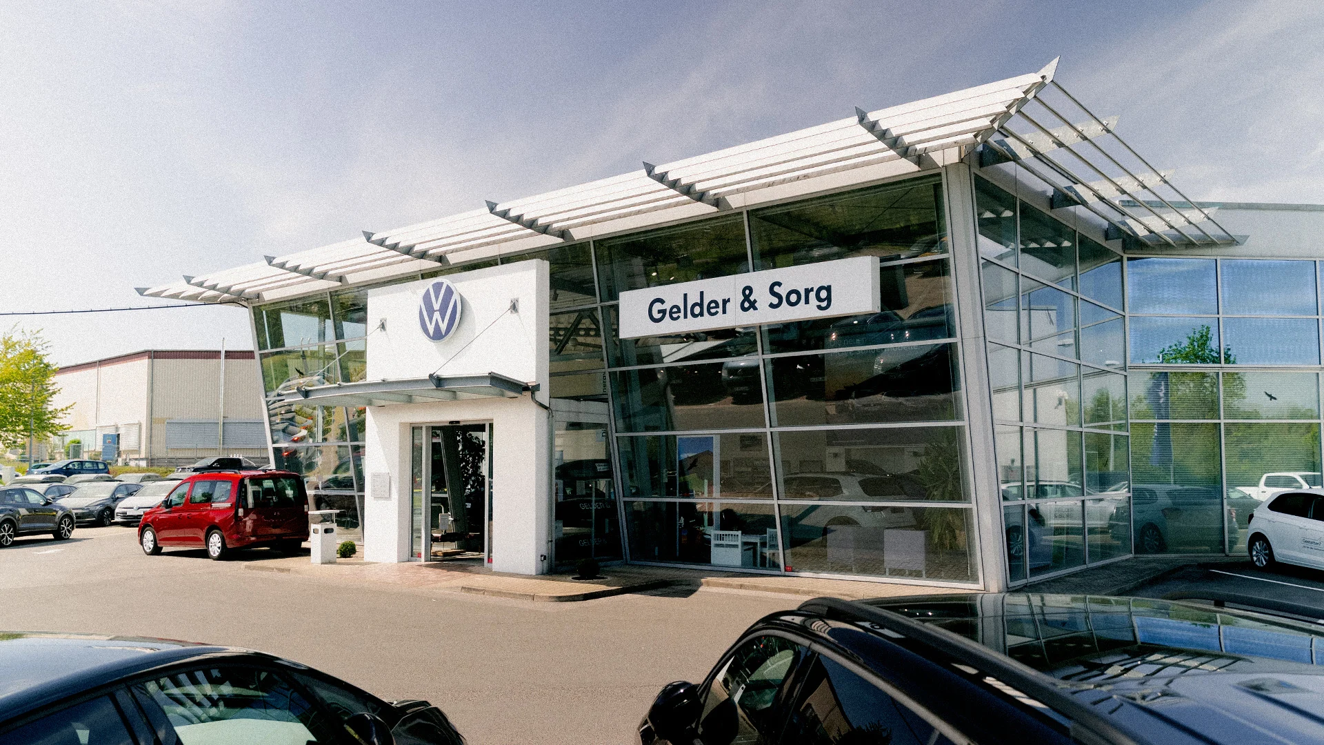 Volkswagen Haßfurt Thumbnail Eine Aufnahme des Volkswagen Autohauses in Haßfurt, die das Gebäude und Volkswagen Fahrzeuge vor dem Gebäude zeigt.