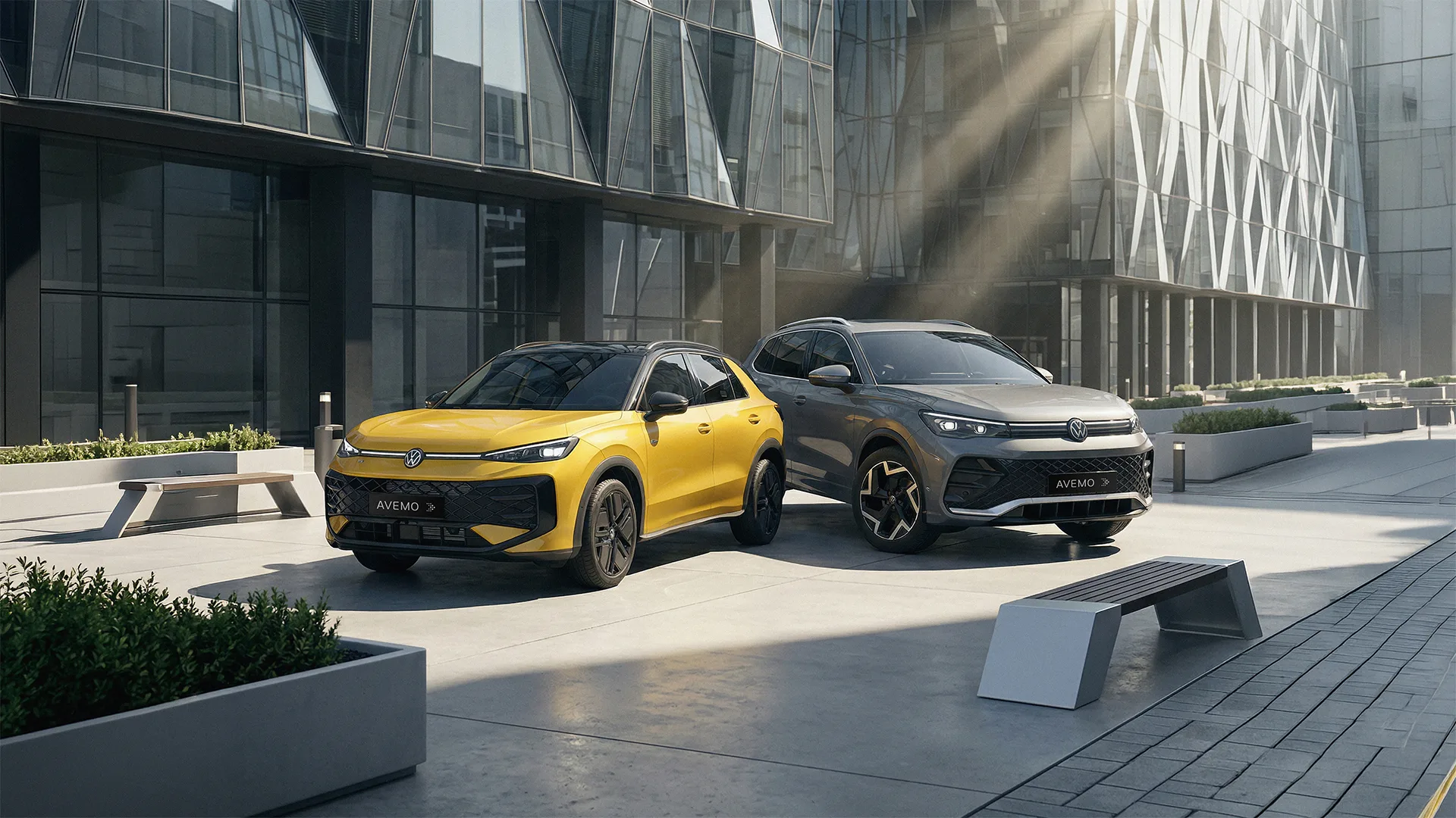 Ein gelber VW T-Roc und ein grauer VW Tiguan parken auf einem modernen, gepflasterten Platz vor einem Gebäude mit Glasfassade. Sonnenstrahlen fallen schräg in das Bild und betonen die AVEMO-Kennzeichen der Fahrzeuge.