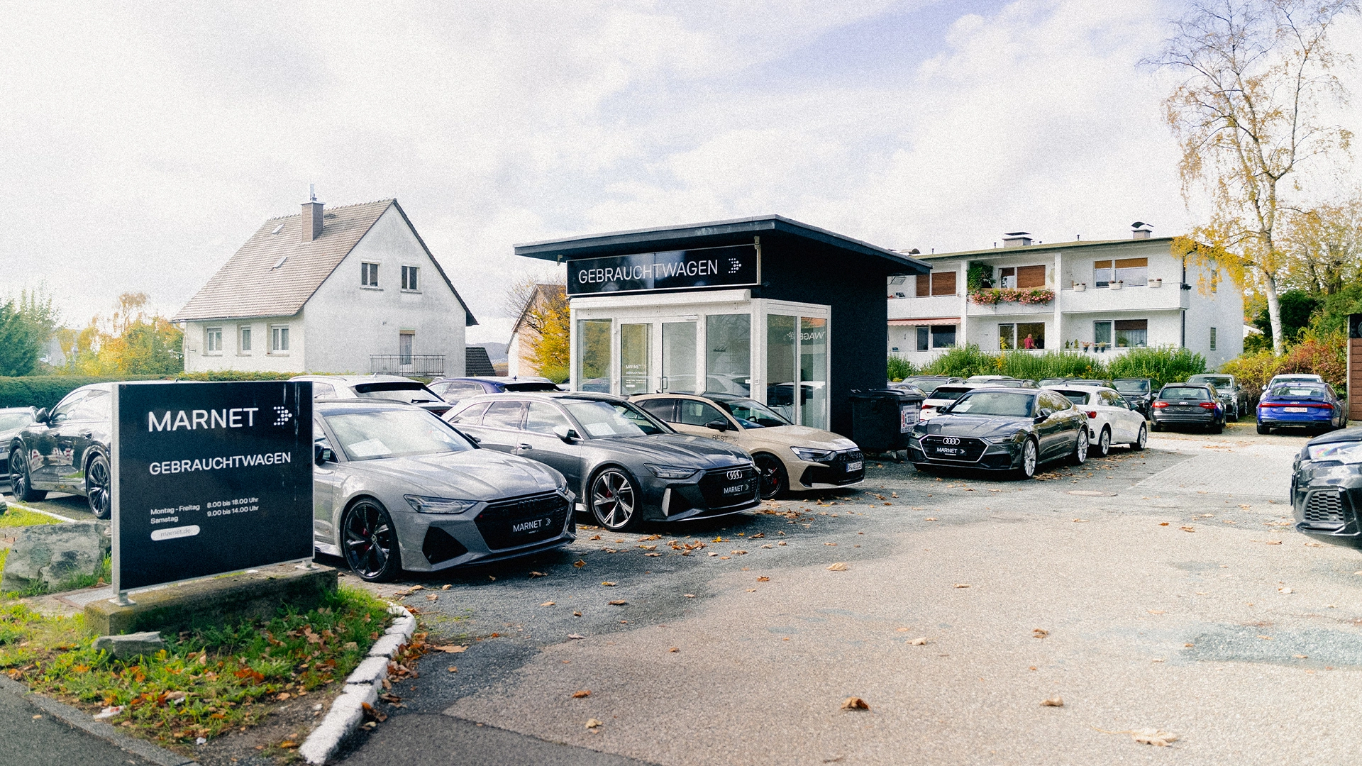 Audi Gebrauchtwagen Königstein im Taunus Header Eine Aufnahme des Audi Gebrauchtwagen Gebäudes in Königstein im Taunus, dass die Gebäude und Audi Fahrzeuge vor dem Gebäude, sowie die Einfahrt zeigt.