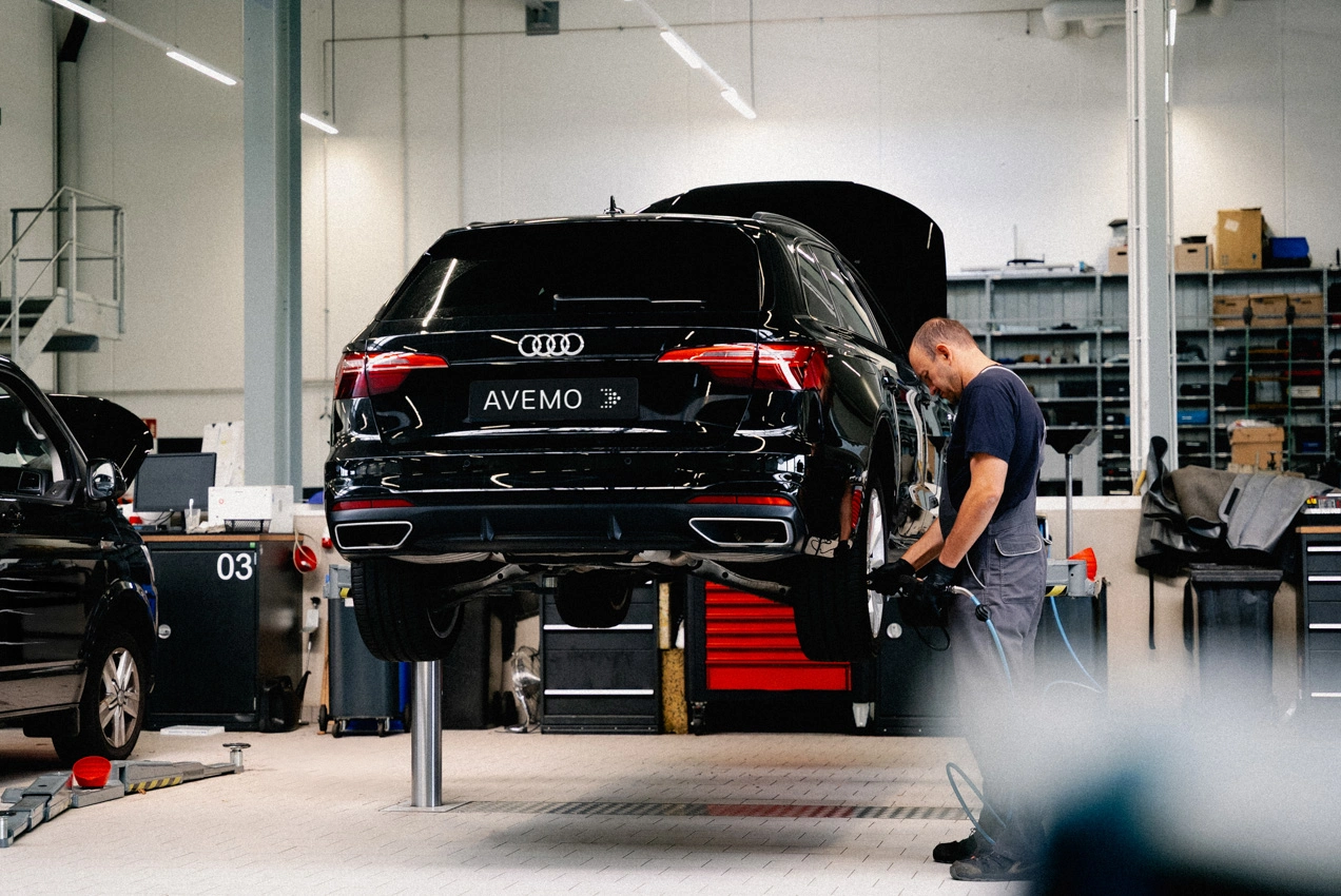 Werkstatt Reifenwechsel m Eine Aufnahme im Reifenlager des Autohauses. Ein Teiledienst-Mitarbeiter in schwarzen AVEMO Polo-Shirt lädt einen Reifen in das Regal ein.