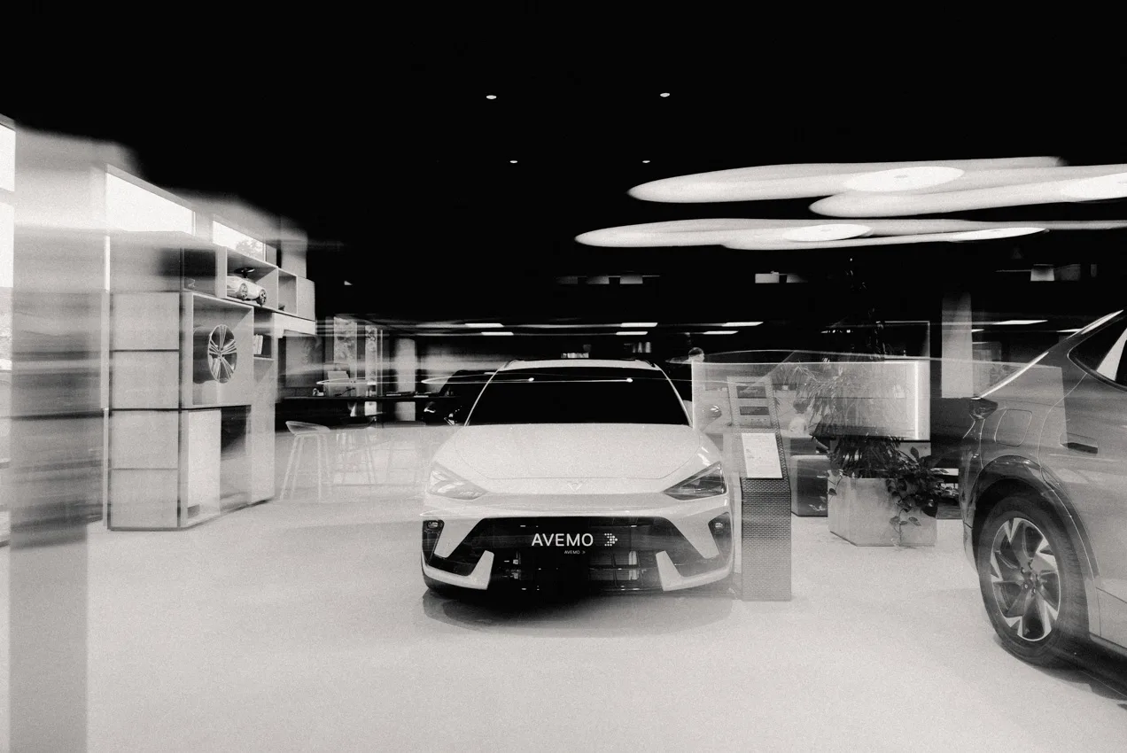 Zu sehen ist eine abstrakte Aufnahme eines CUPRA Leons im Showroom eines Autohauses. Das Bild wurde mit Bewegungsunschärfe aufgenommen und schwarz-weiß eingefärbt.