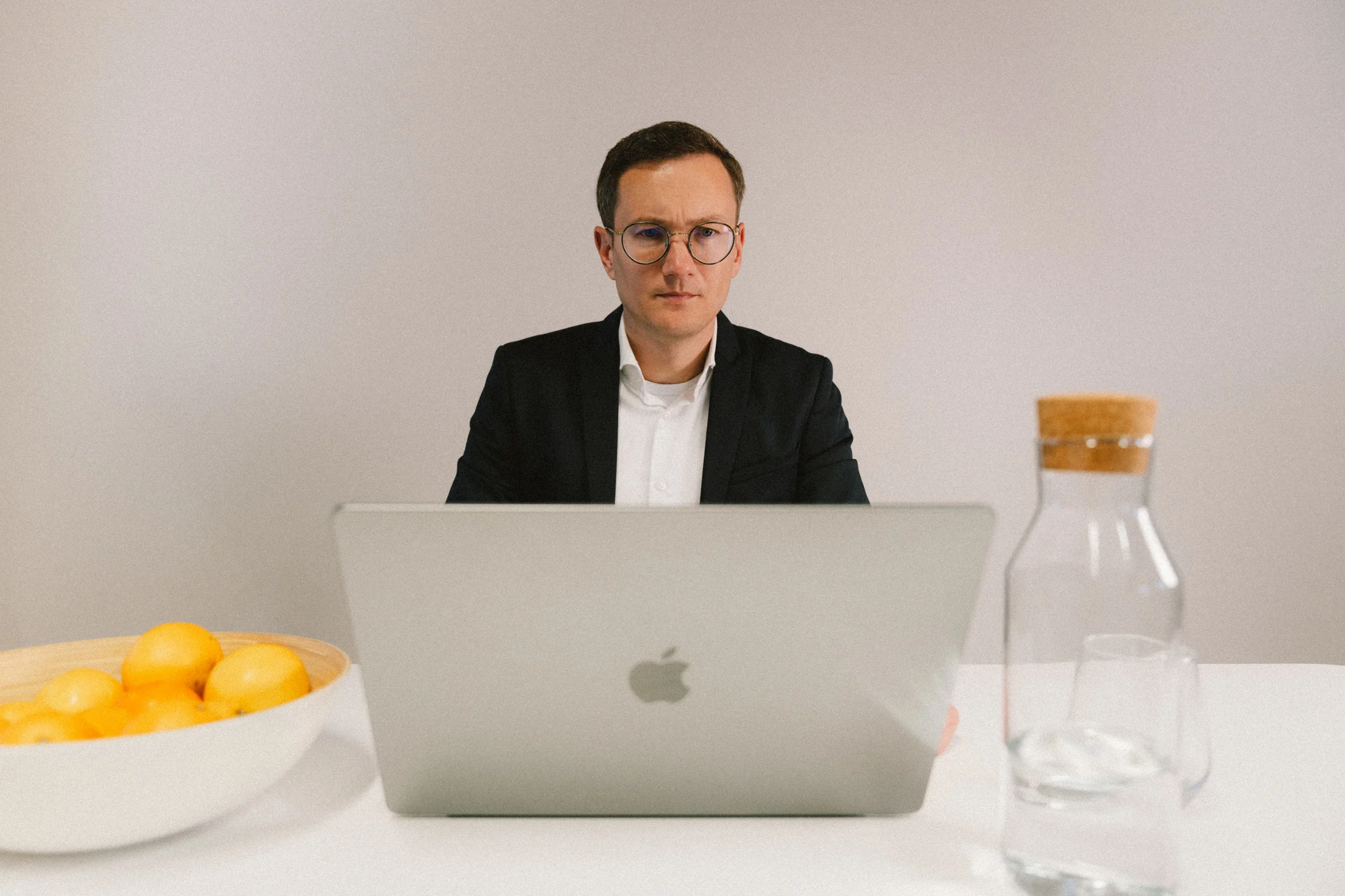 Büro am Laptop m Ein Mann in Anzug sitzt an einem Notebook und arbeitet. Auf dem Tisch steht eine Schale mit Obst und eine Karaffe mit Wasser.
