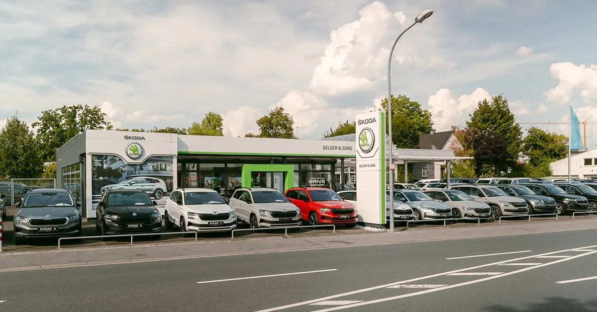 Eine Aufnahme des Škoda und Volkswagen Gebrauchtwagen Autohauses in Haßfurt, die das Gebäude und Škoda Fahrzeuge vor dem Gebäude, sowie die Einfahrt und die Zeiler Straße zeigt.