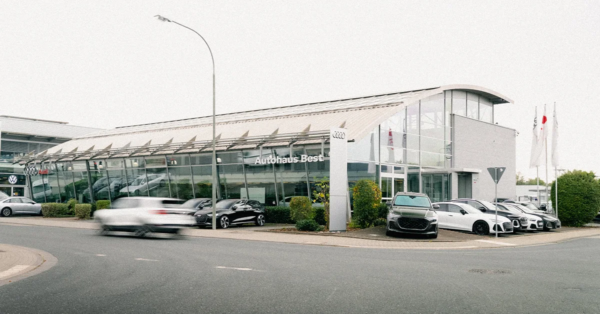 Eine Aufnahme des Audi Autohauses in Mühlheim am Main, die das Gebäude und Audi Fahrzeuge vor dem Gebäude, sowie den Parkplatz zeigt.