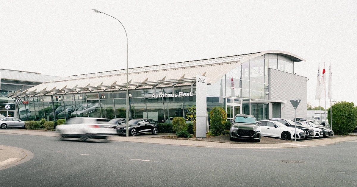 Eine Aufnahme des Audi Autohauses in Mühlheim am Main, die das Gebäude und Audi Fahrzeuge vor dem Gebäude, sowie den Parkplatz zeigt.