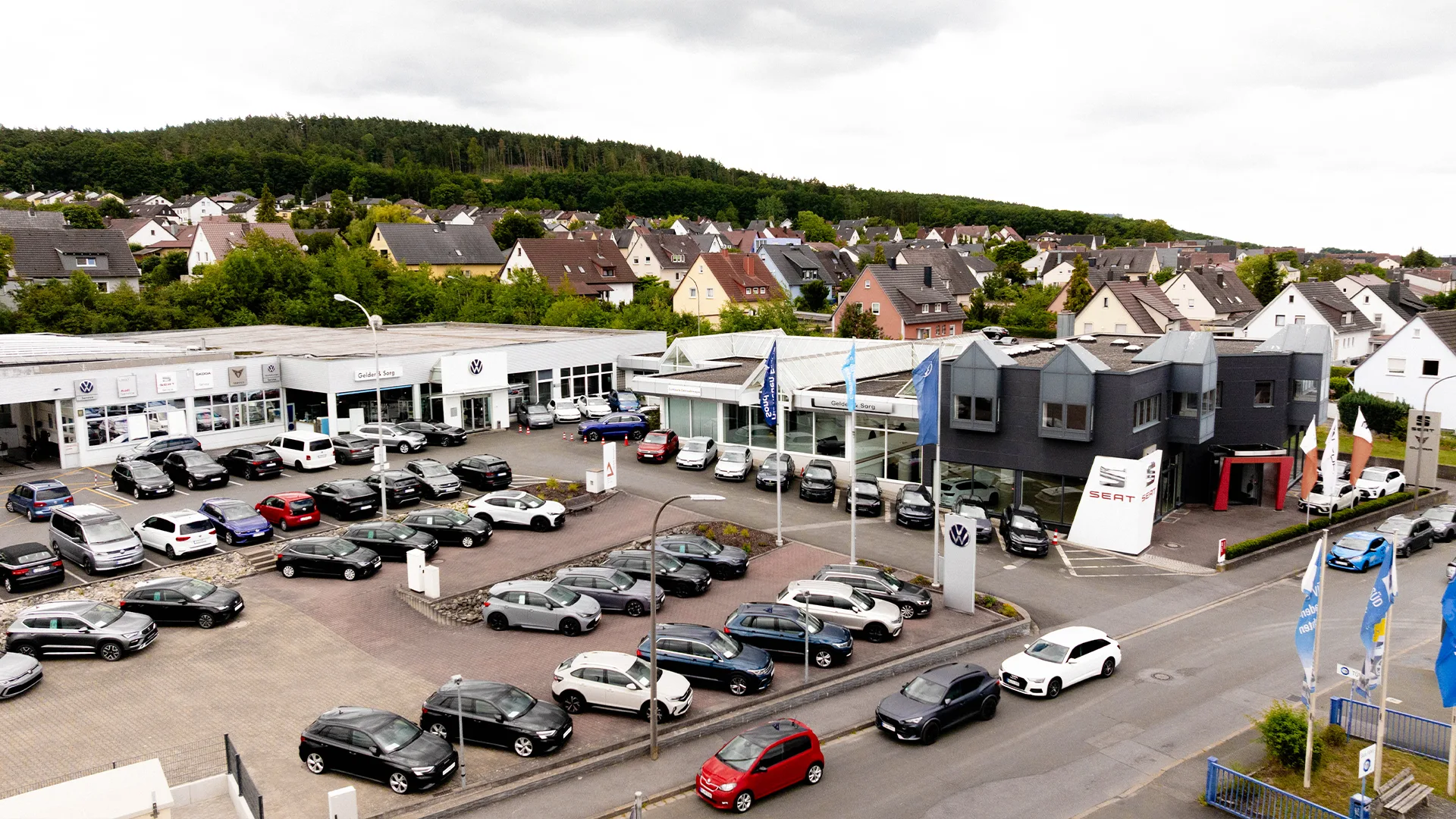 Eine Aufnahme des Volkswagen Autohauses in Lichtenfels, die das VW-Gebäude, den Hof sowie die Volkswagen Fahrzeuge vor dem Autohaus zeigt.