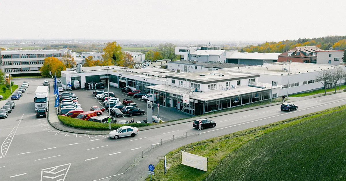 Eine Aufnahme des Volkswagen Autohauses in Kelkheim, die das Gebäude und Volkswagen Fahrzeuge vor dem Gebäude, sowie Parkplätze und die Dieselstraße zeigt.
