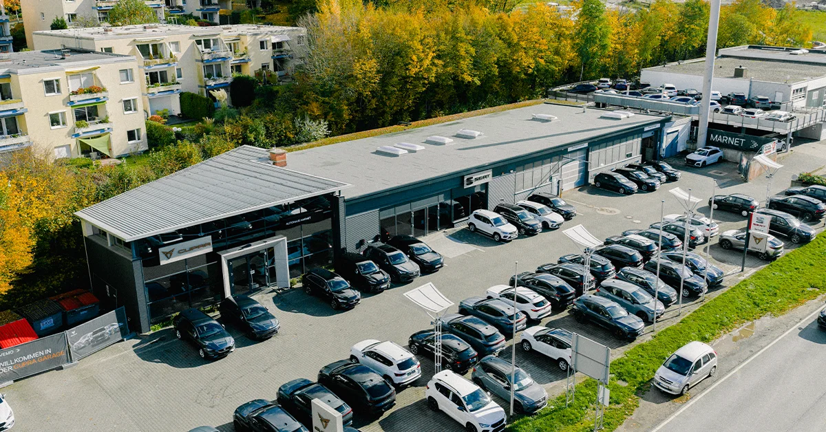 Eine Aufnahme des SEAT & CUPRA Autohauses in Königstein im Taunus, die das Gebäude und SEAT und CUPRA Fahrzeuge vor dem Gebäude, sowie die Einfahrt zeigt.