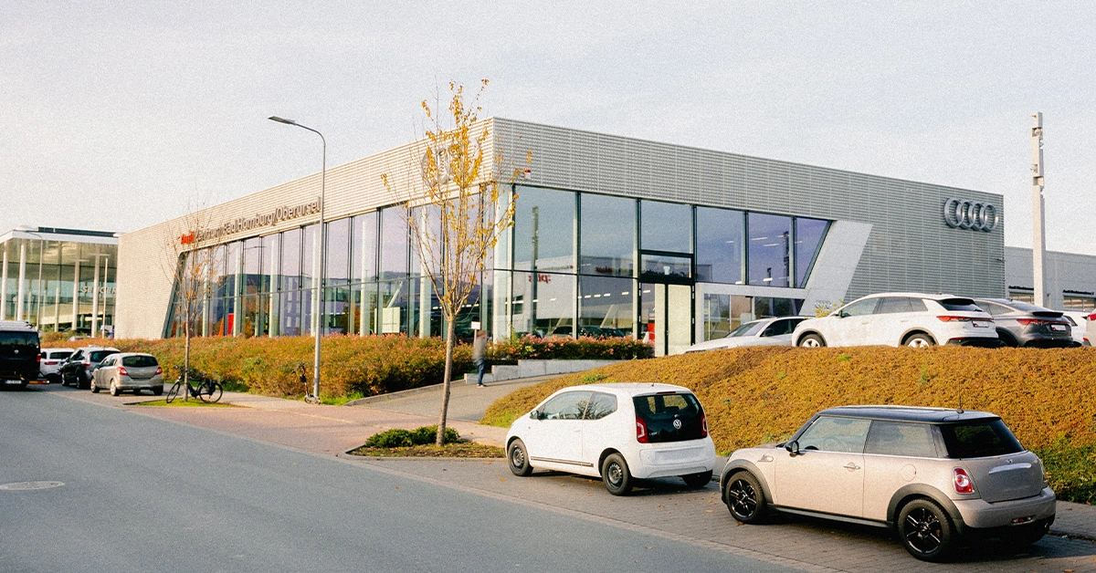 Eine Aufnahme des Audi Zentrums in Bad Homburg / Oberursel, die das Gebäude und Audi Fahrzeuge vor dem Gebäude, sowie die Einfahrt zeigt.