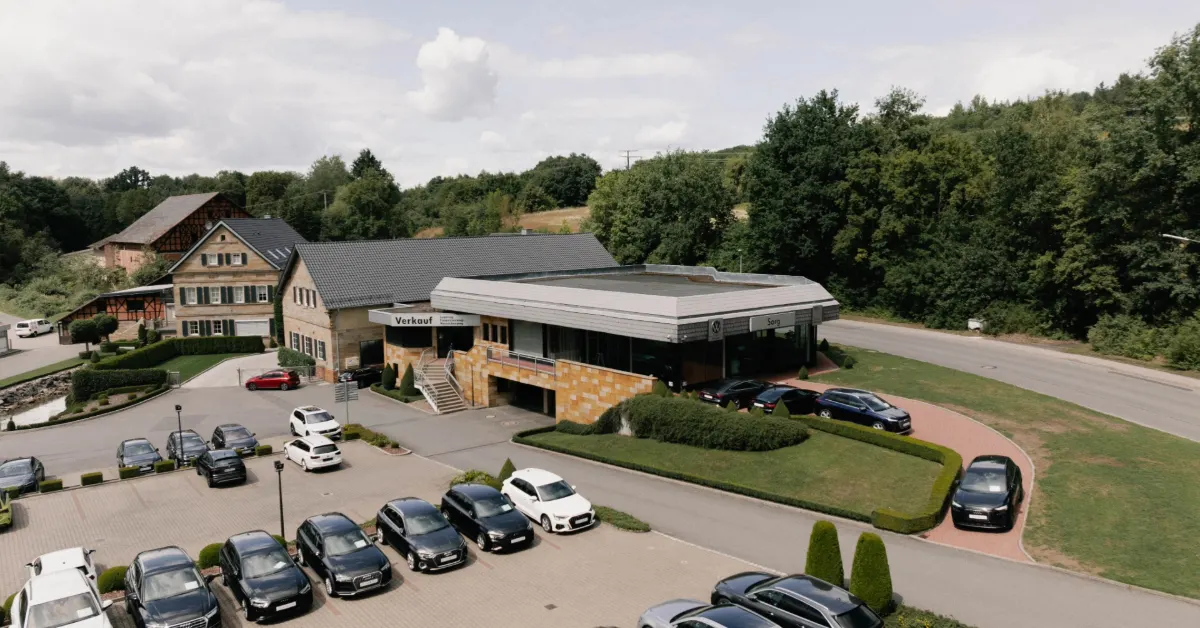 Eine Aufnahme des Gelder & Sorg Autohauses in Ebern, die das Gebäude und Fahrzeuge vor dem Gebäude sowie die Einfahrt zeigt.