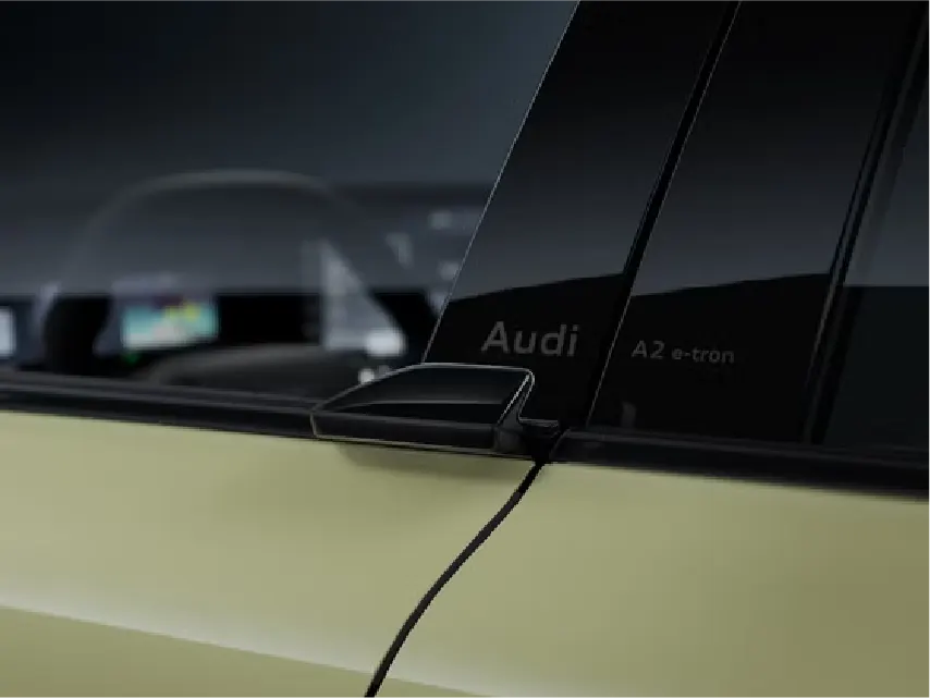 Nahaufnahme der B-Säule eines hellgrünen Audi A2 e-tron mit schwarzem Schriftzug „Audi A2 e-tron“ auf der Scheibenverkleidung und einem kompakten, schwarzen Außenspiegel.