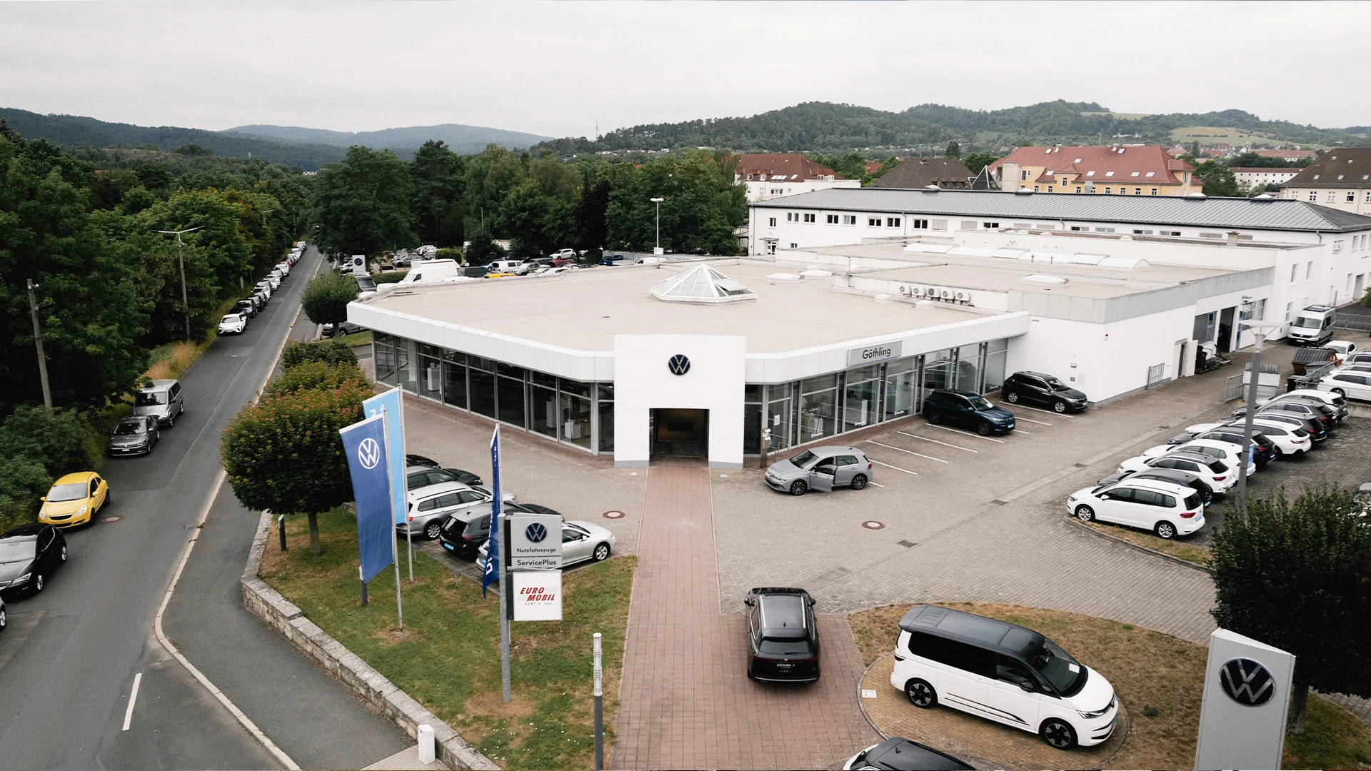 Eine Aufnahme des Volkswagen und Volkswagen Nutzfahrzeuge Autohauses in Eisenach, dass das Gebäude und Volkswagen Fahrzeuge vor dem Gebäude, sowie die Einfahrt zeigt.