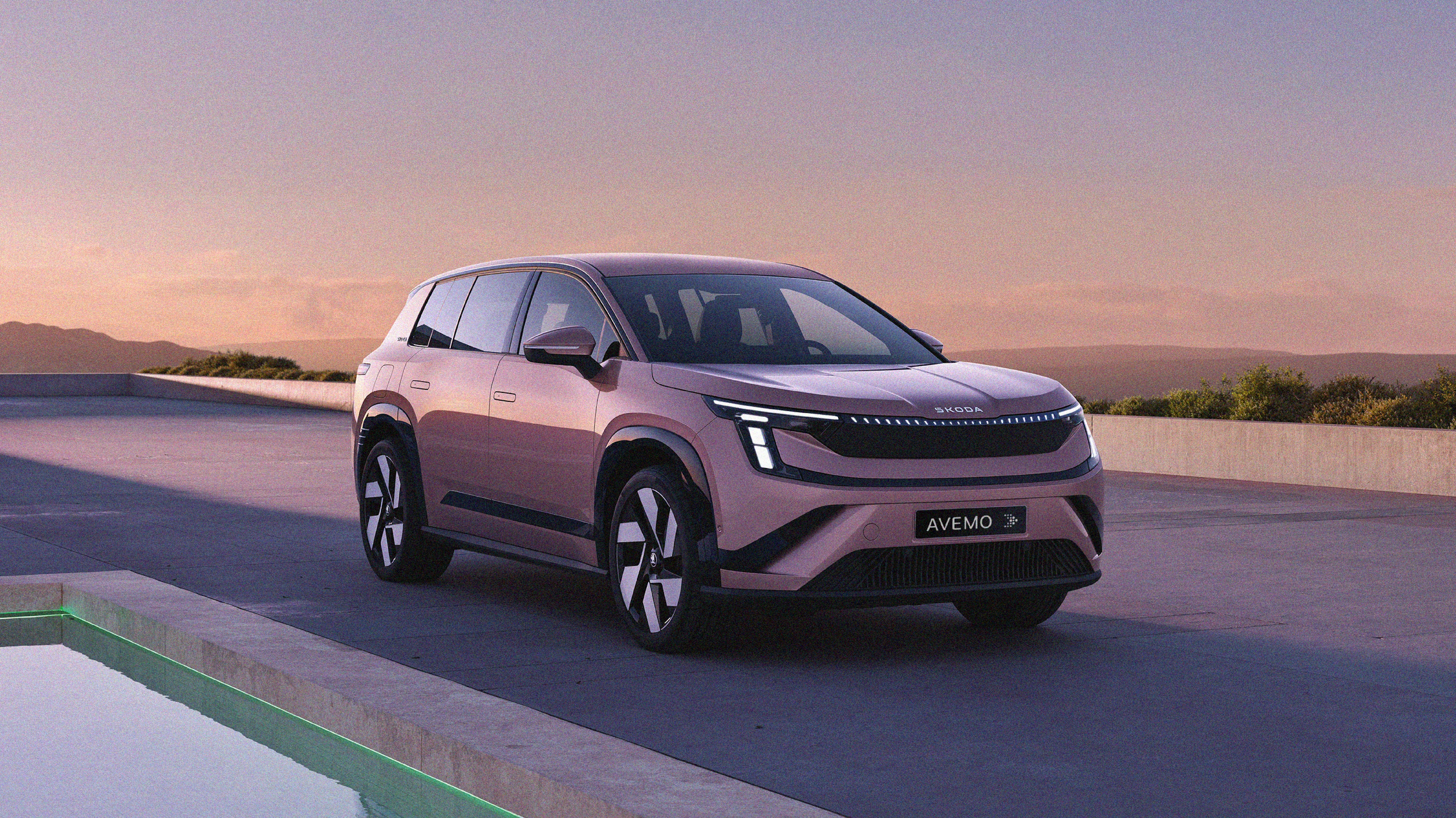 Ein moderner, rosé-metallicfarbener Škoda Elroq SUV steht bei Sonnenuntergang auf einer Terrasse mit Pool. Das Auto zeigt markante LED-Scheinwerfer und das Kennzeichen „AVEMO“. Im Hintergrund sind Hügel unter einem sanften, abendlichen Himmel zu sehen.