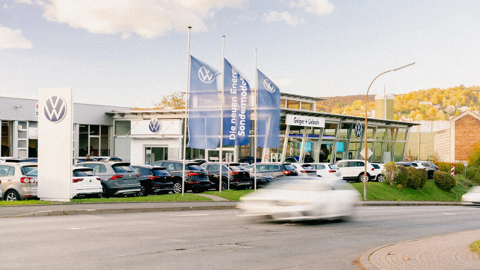 Eine Aufnahme des Volkswagen Autohauses in Linsengericht, dass das Gebäude und Volkswagen Fahrzeuge vor dem Gebäude, sowie die Gelnhäuser Straße zeigt.