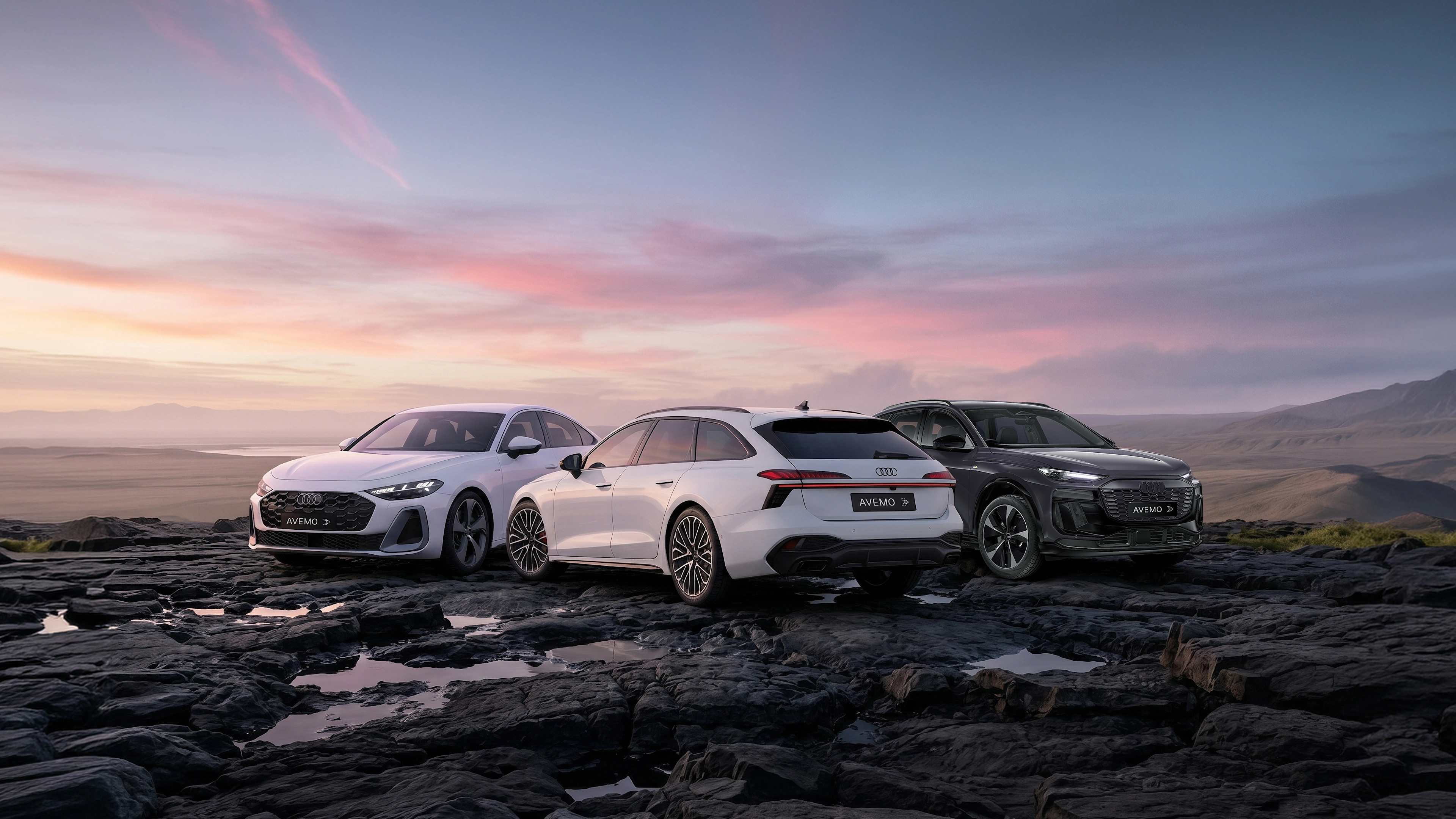 Drei moderne Audi-Modelle – eine weiße Limousine, ein weißer Kombi und ein dunkler SUV – mit AVEMO-Kennzeichen parken auf dunklem, felsigem Terrain. Im Hintergrund erstreckt sich eine weite Landschaft unter einem farbenfrohen Abendhimmel.