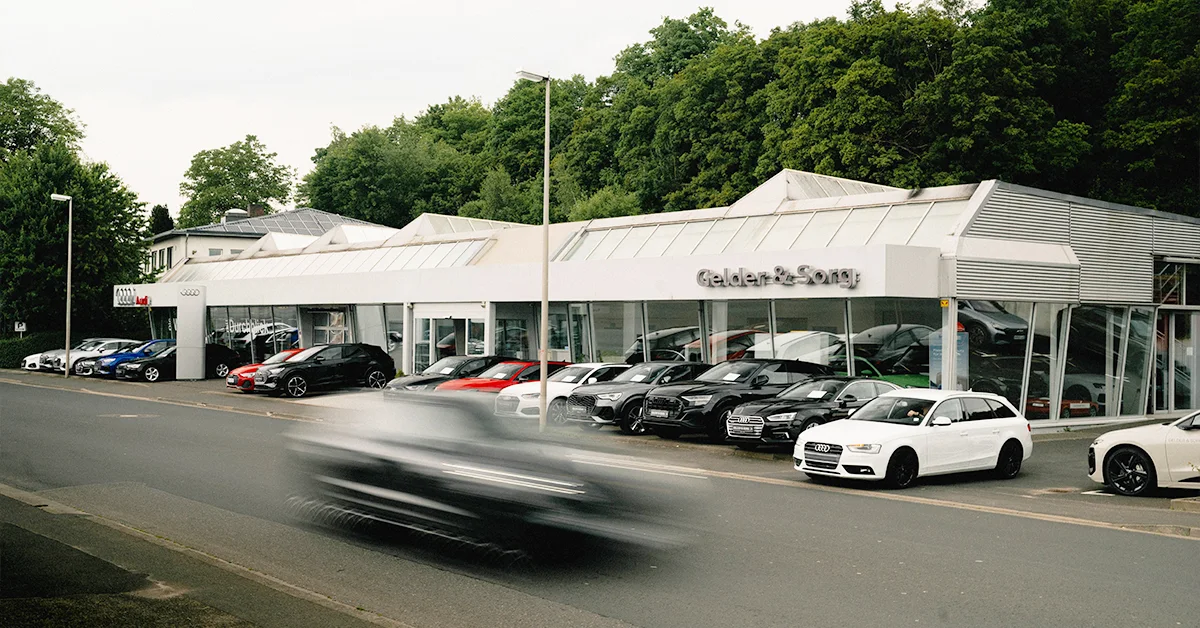 Eine Aufnahme des Audi Autohauses in Bad Kissingen, die das Gebäude und Audi Fahrzeuge vor dem Gebäude, sowie die Würzburger Straße zeigt.