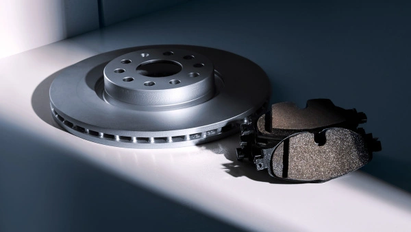 Eine neue, silberne Bremsscheibe liegt neben zwei schwarzen Bremsbelägen auf einer hellen Oberfläche. Die Fahrzeugteile sind durch einen markanten Licht-Schatten-Kontrast professionell in Szene gesetzt.