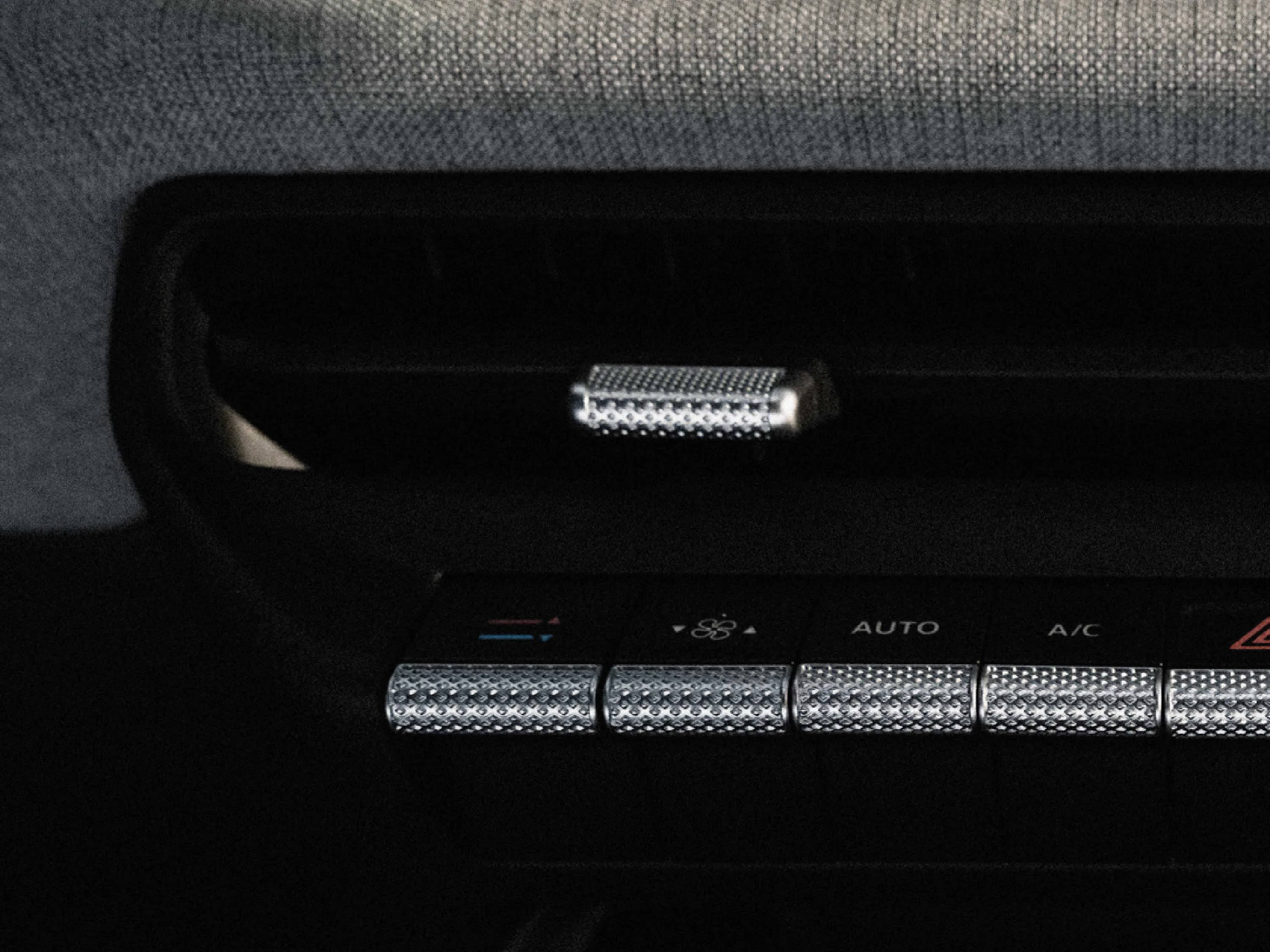 Nahaufnahme der Mittelkonsole im VW ID.Polo. Zu sehen sind hochwertige, silbern strukturierte Kippschalter für die Klimasteuerung (u. a. Auto, A/C) sowie ein passender Regler an der darüberliegenden Lüftungsdüse vor dunklem Hintergrund.