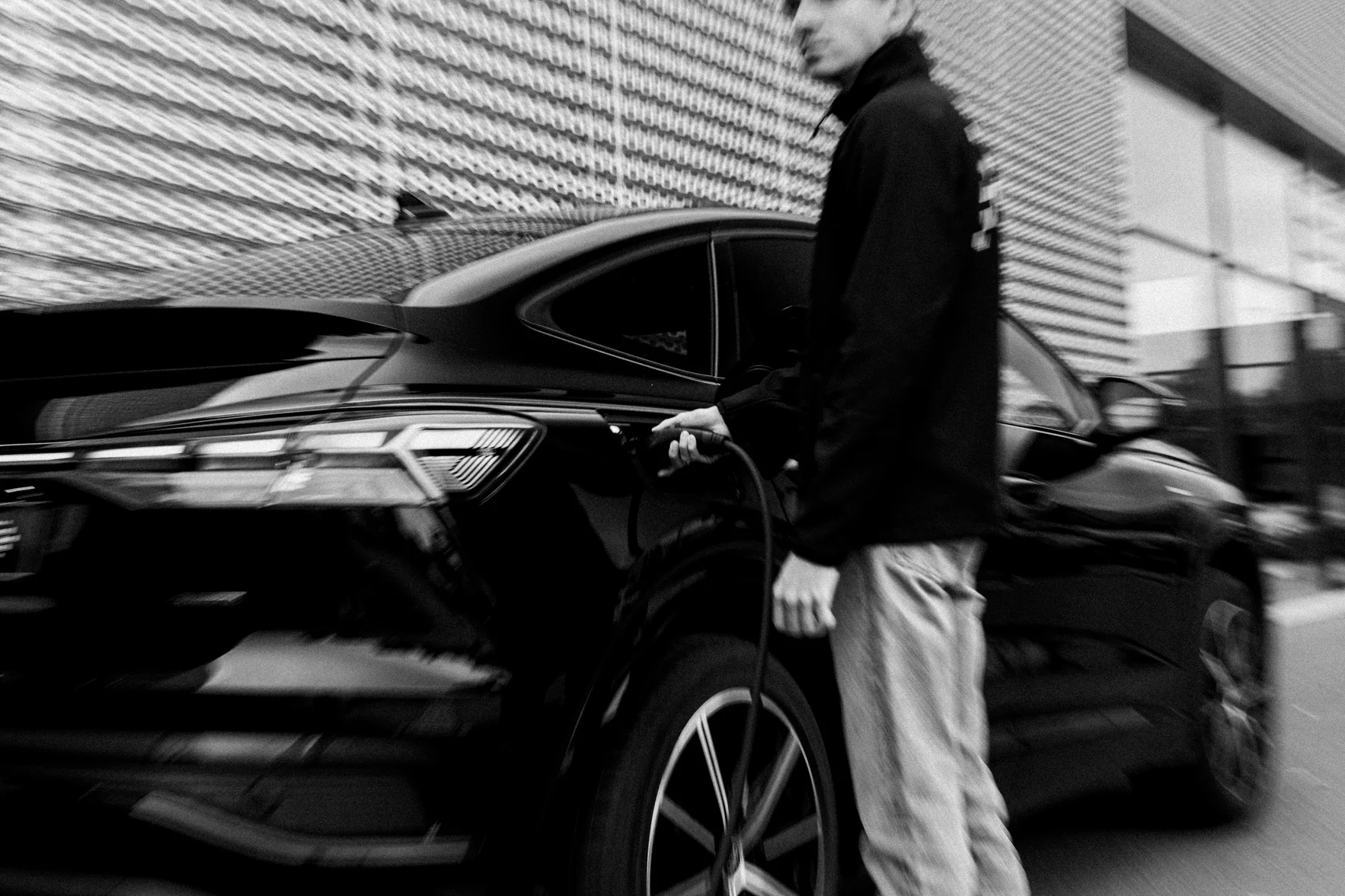 Eine Aufnahme einer offenen Ladebuchse eines E-Autos. Eine Person, die neben dem Auto steht, schließt gerade ein Ladekabel an, um den Ladevorgang zu starten.