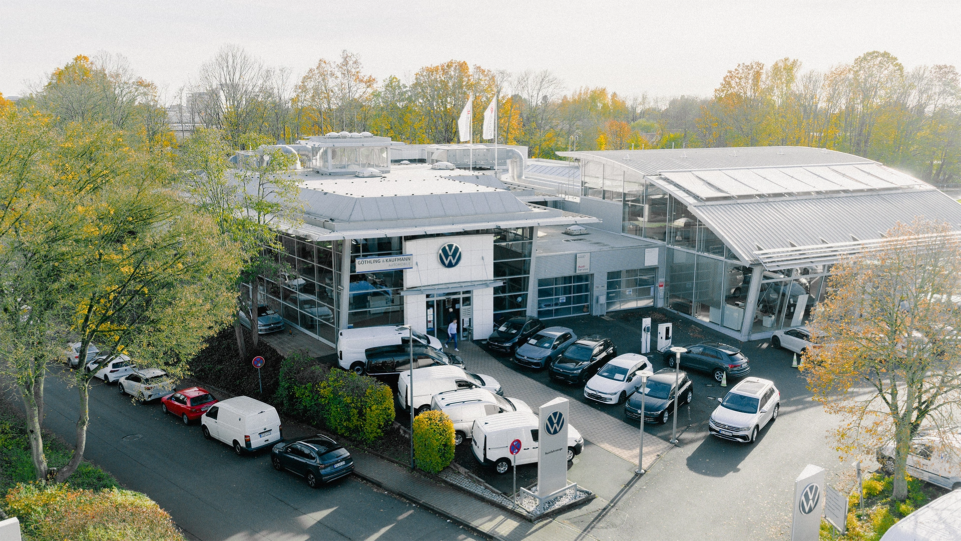 Volkswagen & Volkswagen Nutzfahrzeuge Eschborn Header Eine Aufnahme des Volkswagen und Volkswagen Nutzfahrzeuge Autohauses in Eschborn, dass die Gebäude und Volkswagen Fahrzeuge vor dem Gebäude, sowie die Einfahrt zeigt.