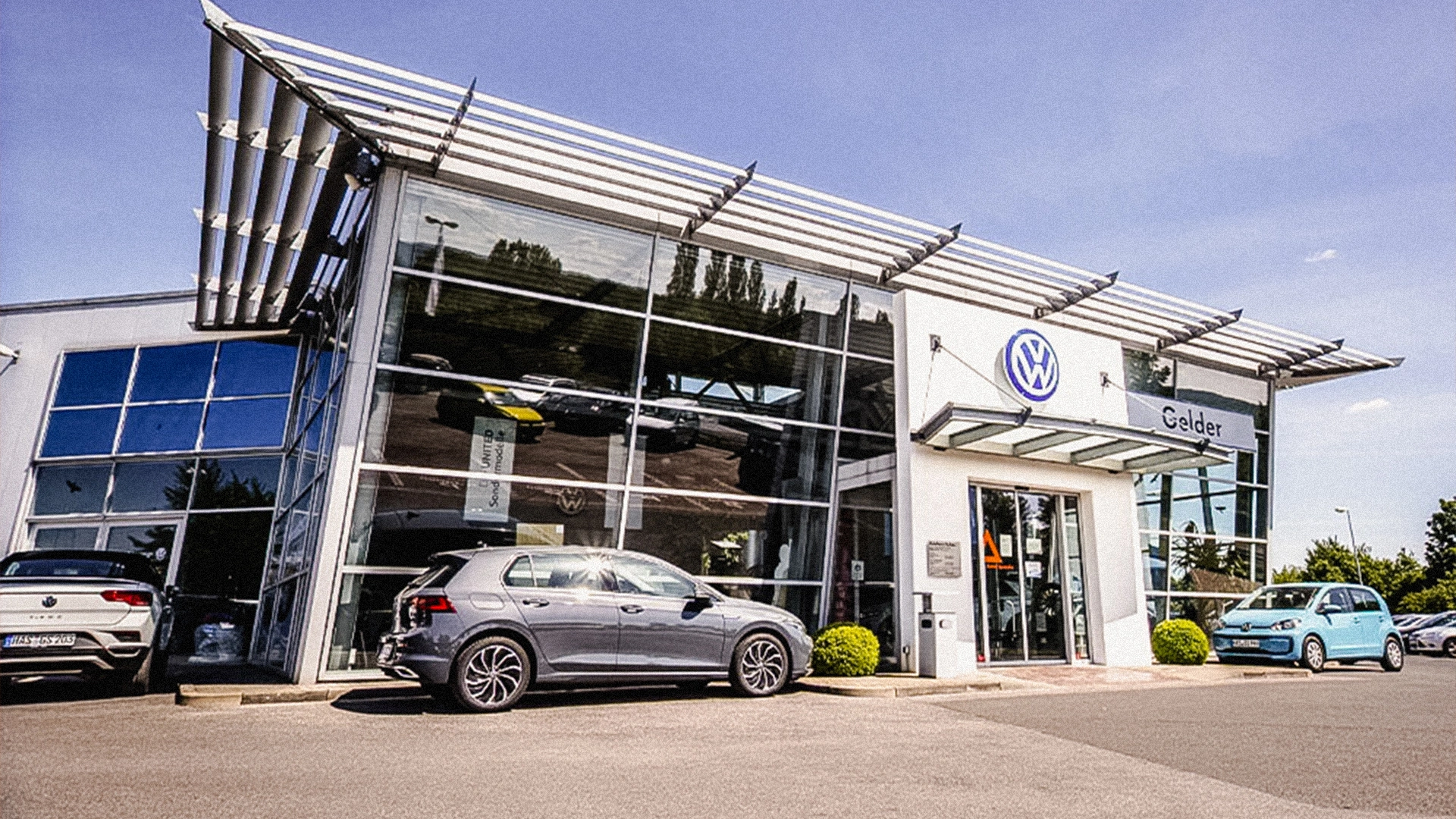 Volkswagen Haßfurt Header Eine Aufnahme des Volkswagen Autohauses in Haßfurt, die das Gebäude und Volkswagen Fahrzeuge vor dem Gebäude zeigt.