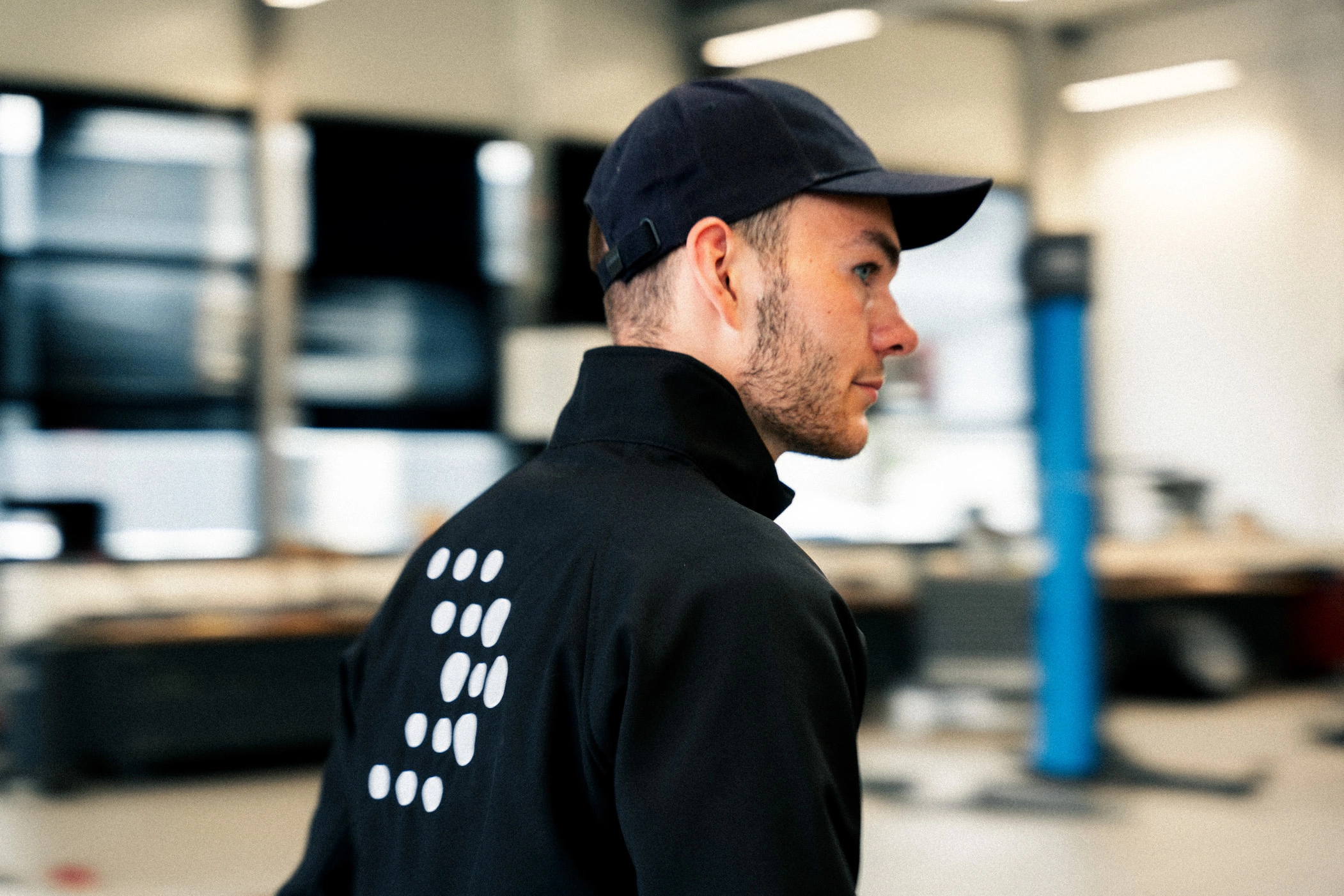 Ein Mann mit schwarzer AVEMO-Jacke und einer Kappe läuft durch die Werkstatt des Autohauses.