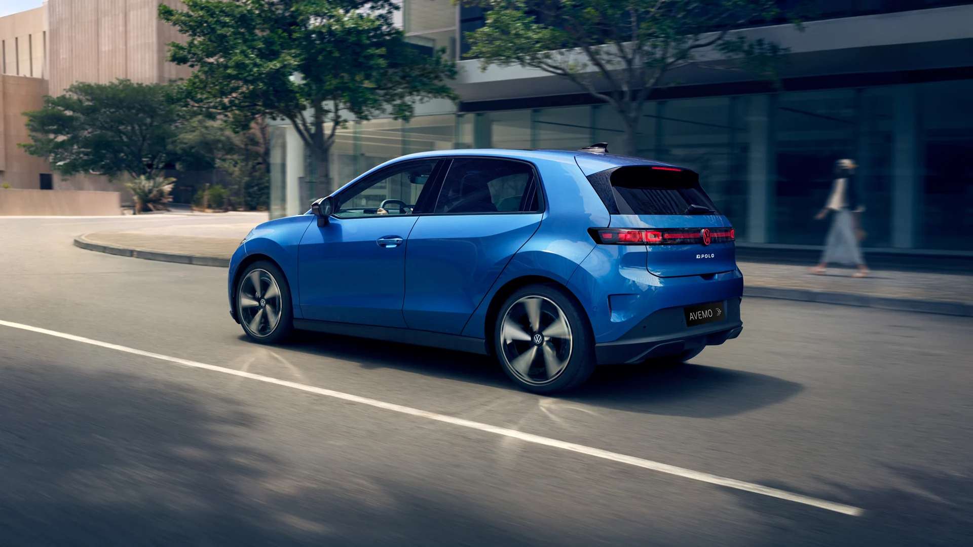 Ein blauer VW ID.Polo mit AVEMO-Kennzeichen fährt dynamisch durch eine moderne Stadtlandschaft. Die Rückansicht zeigt das markante durchgehende LED-Lichtband und das beleuchtete Logo vor einer Kulisse aus Glasgebäuden und Bäumen.