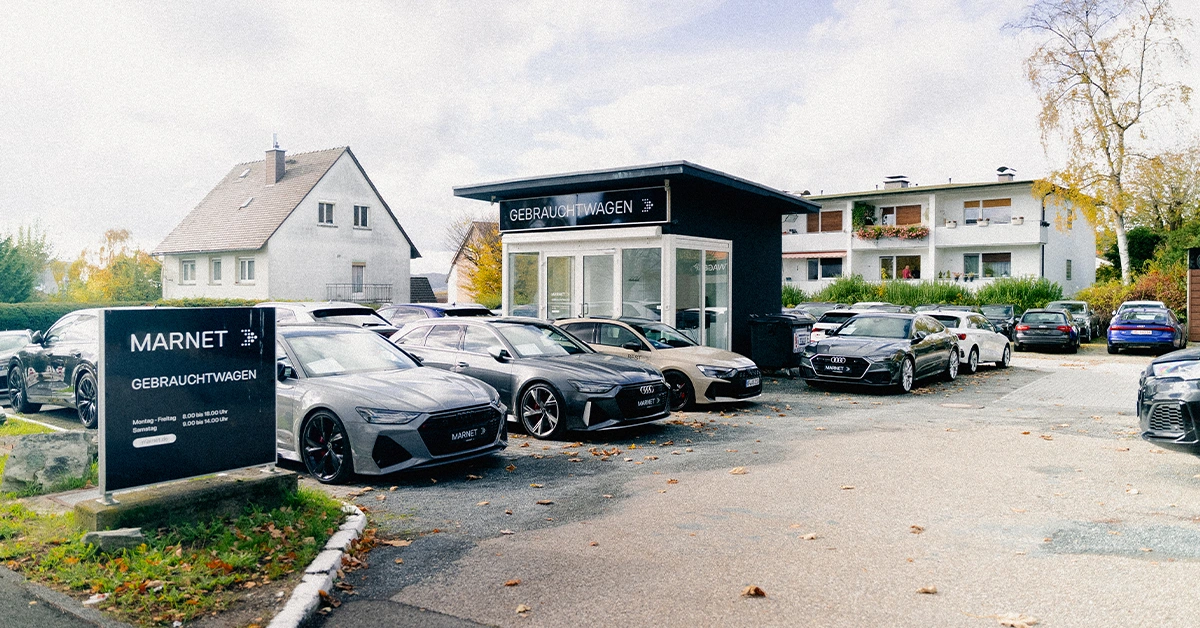 Eine Aufnahme des Audi Gebrauchtwagen Gebäudes in Königstein im Taunus, die das Gebäude und Audi Fahrzeuge vor dem Gebäude, sowie die Einfahrt zeigt.