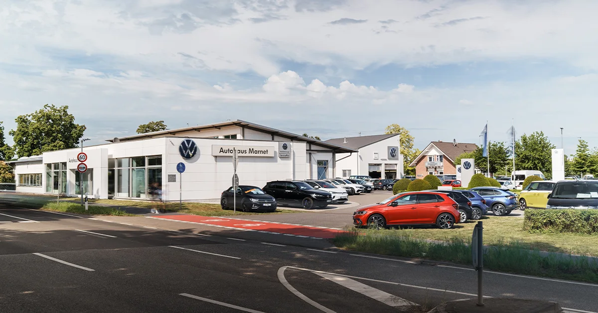 Eine Aufnahme des Volkswagen Autohauses in Bad Nauheim, dass das Gebäude und Volkswagen Fahrzeuge vor dem Gebäude, sowie die Friedberger Straße zeigt.